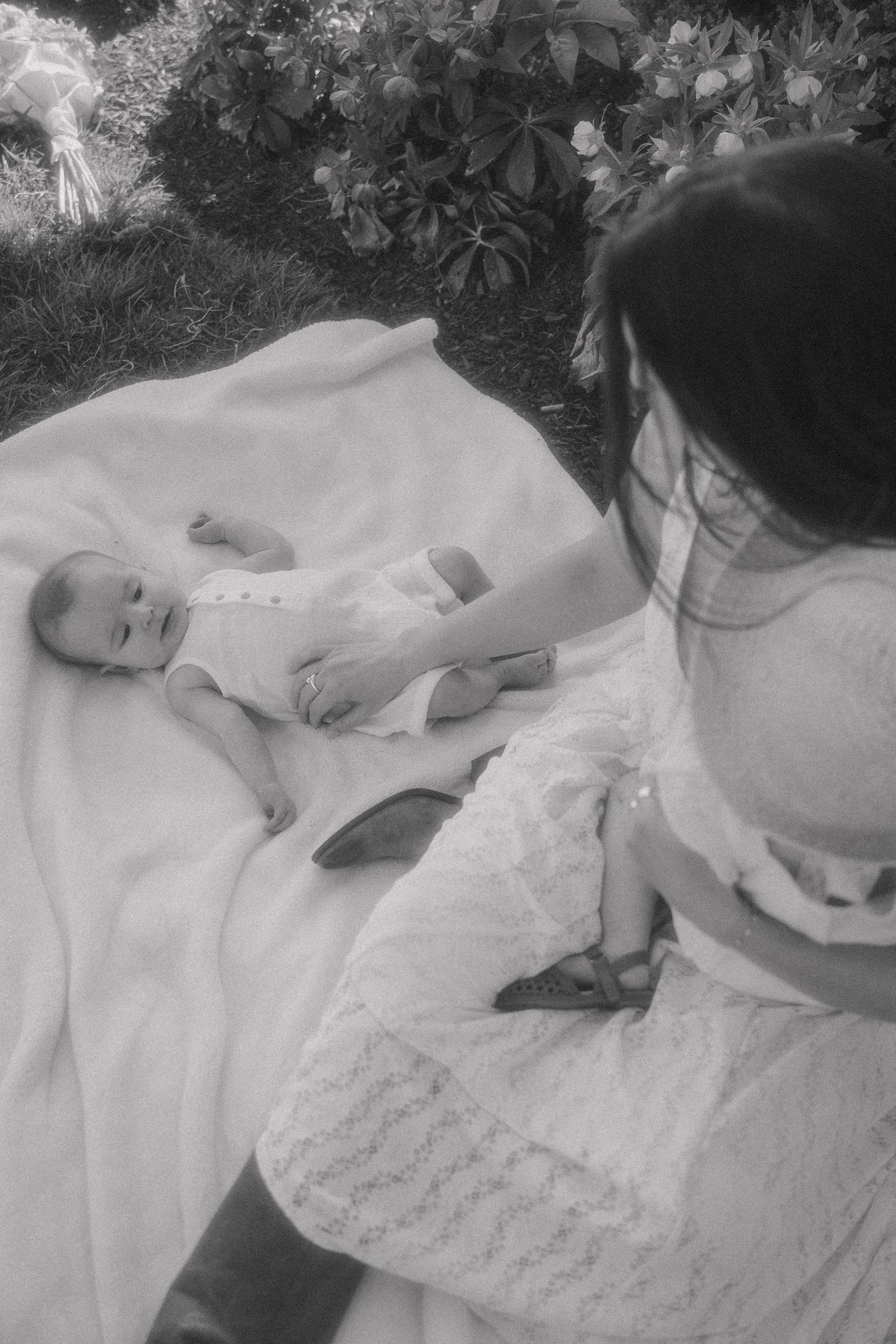 Black and white photo of a mother in lace dress looking at her newborn baby on a white blanket.