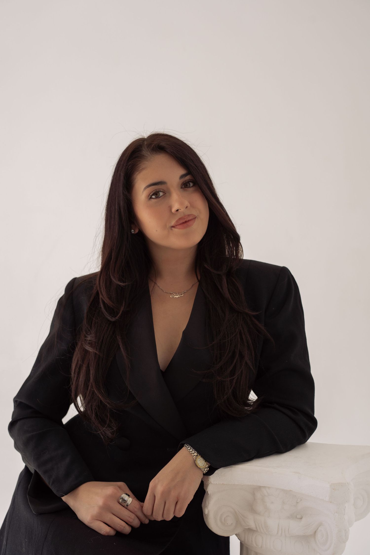 Young woman in black blazer suit posing confidently against a white studio background.