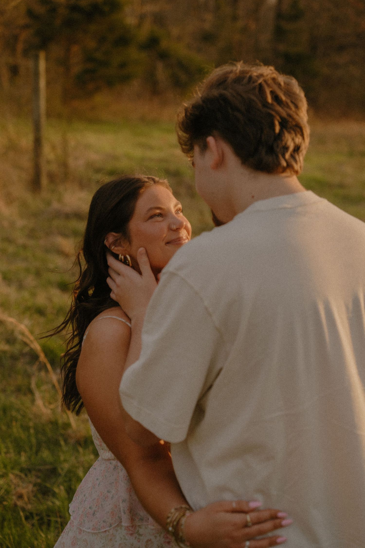 Young couple sharing a tender moment at sunset in a grassy field, man cupping woman's face.