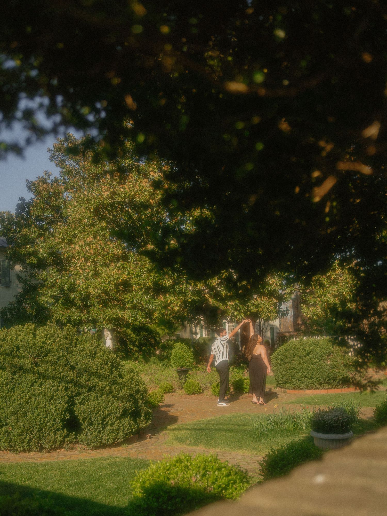 Couple sharing a romantic moment in a lush garden surrounded by trimmed hedges and trees.