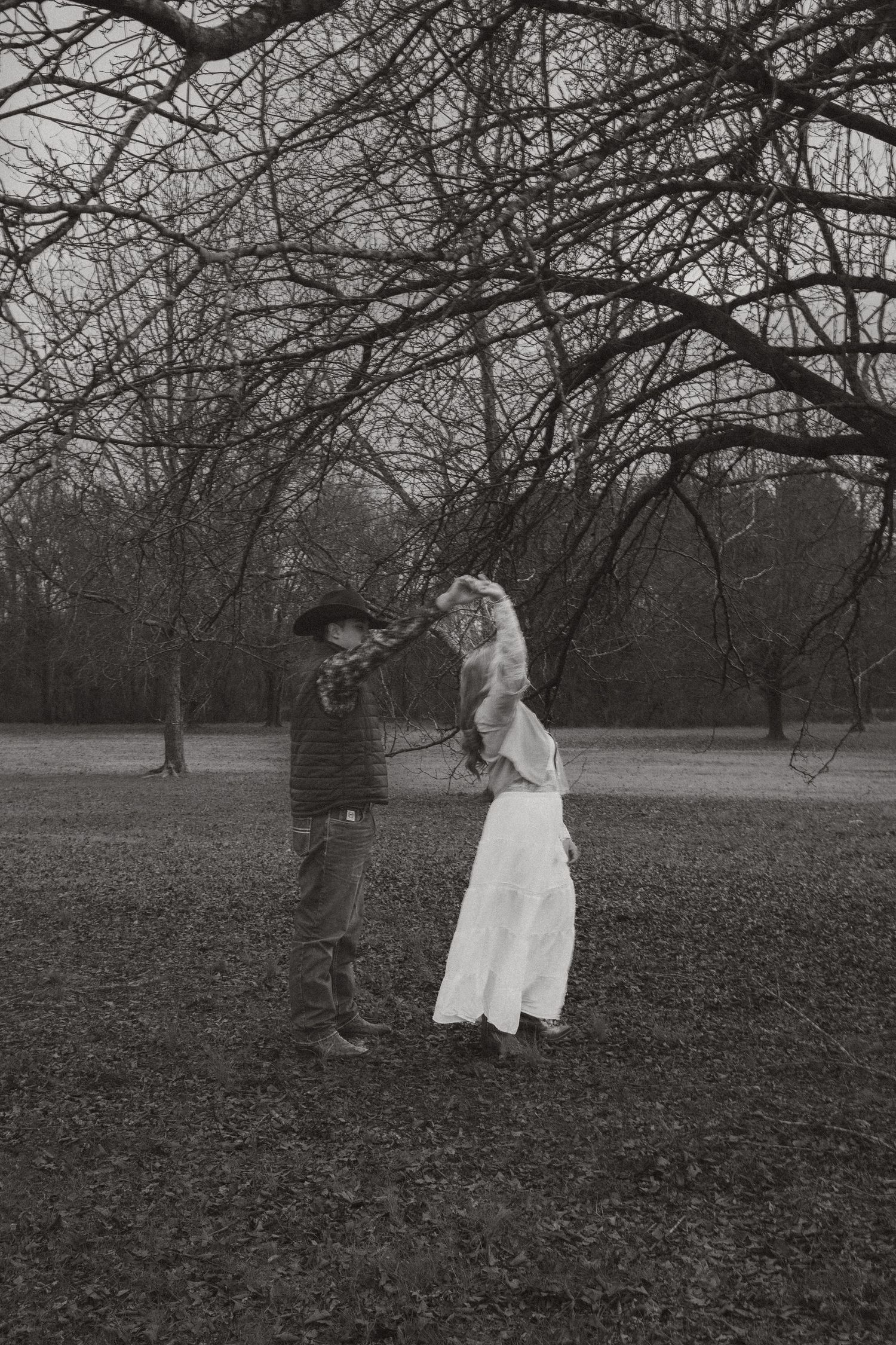 Black and white photo of couple dancing under bare trees in an outdoor winter setting.