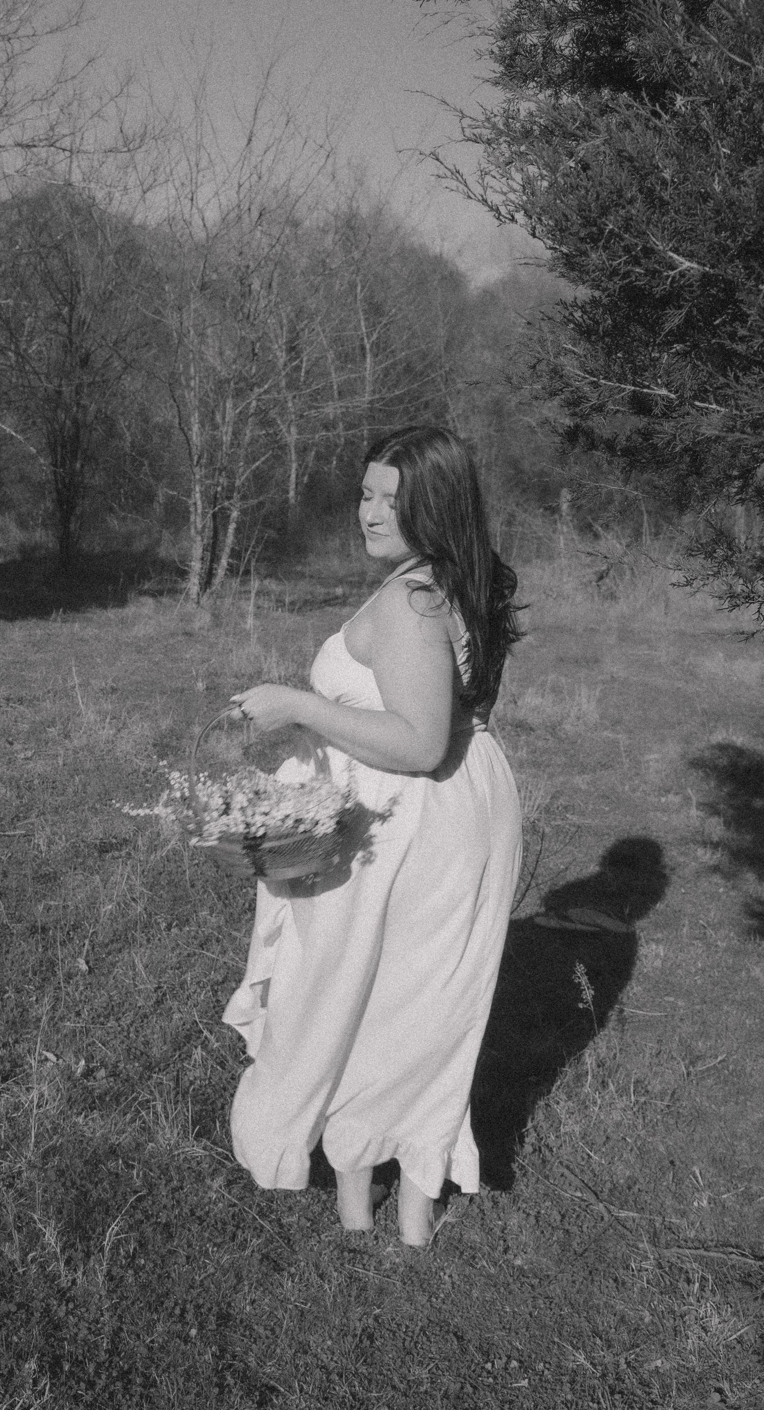 Black and white photo of a woman in a white dress holding a flower basket outdoors.