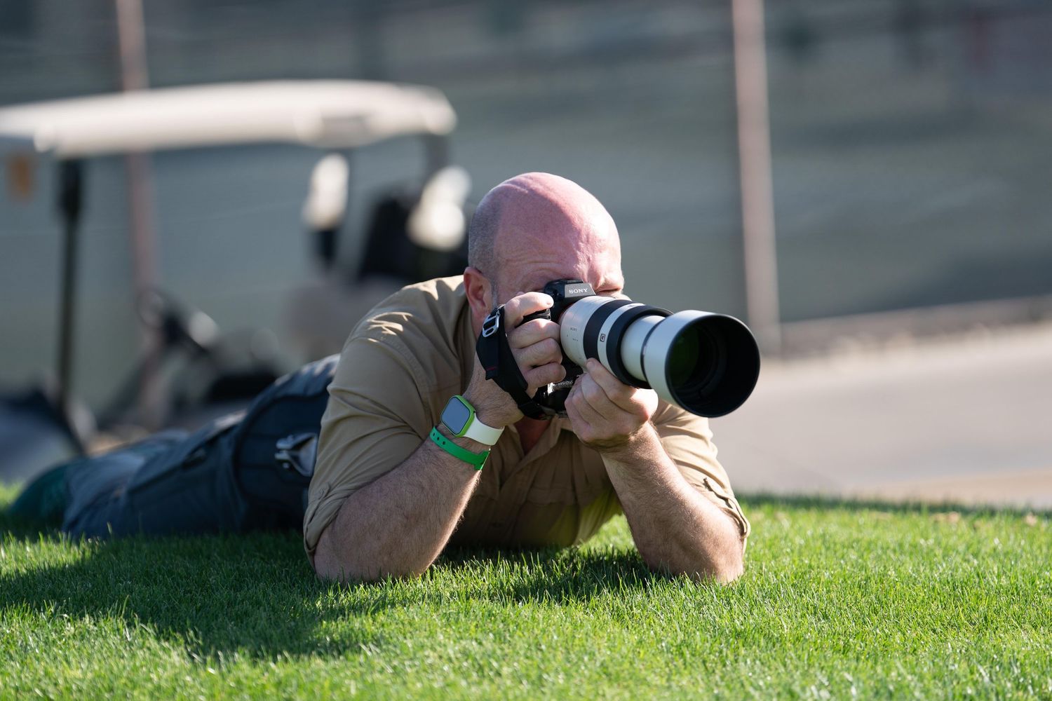 Owner of Mountain Productions laying on a golf course taking a photograph with a large lens.