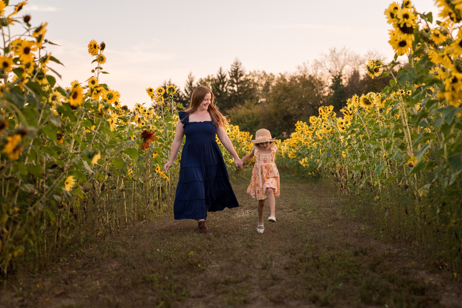 Mother and daughter holding hangs in sunflower field at golden hour sunset during family photo session in Medford, Burlington County, NJ