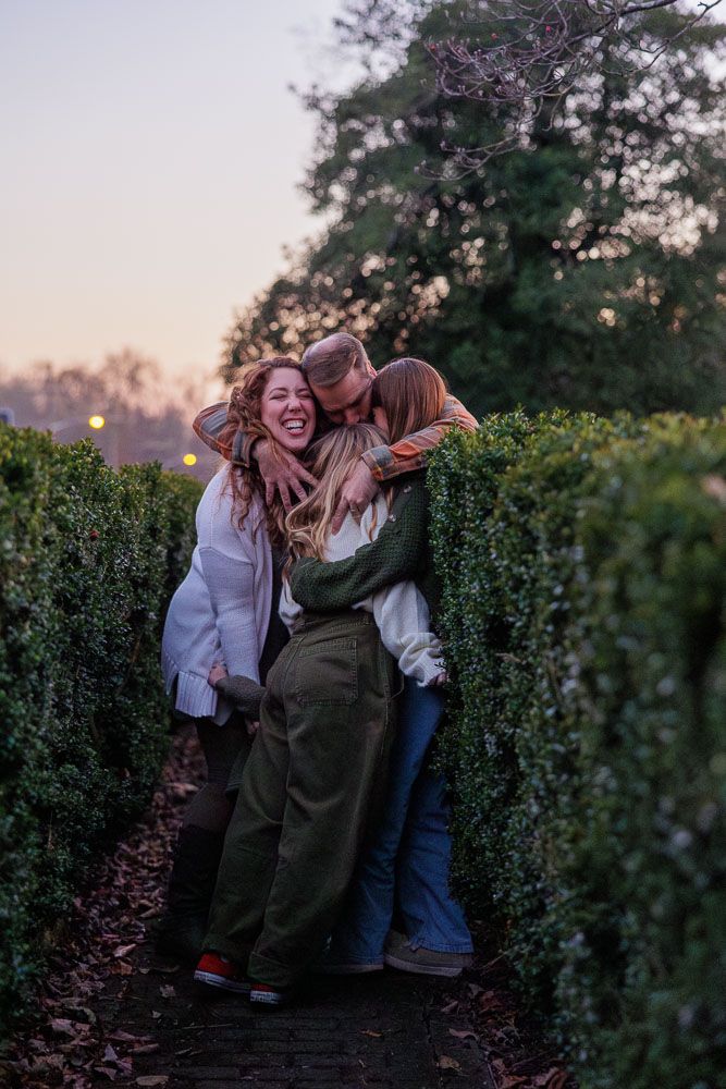 A couple shares joyful moments together while posing outdoors at sunset among green hedges.