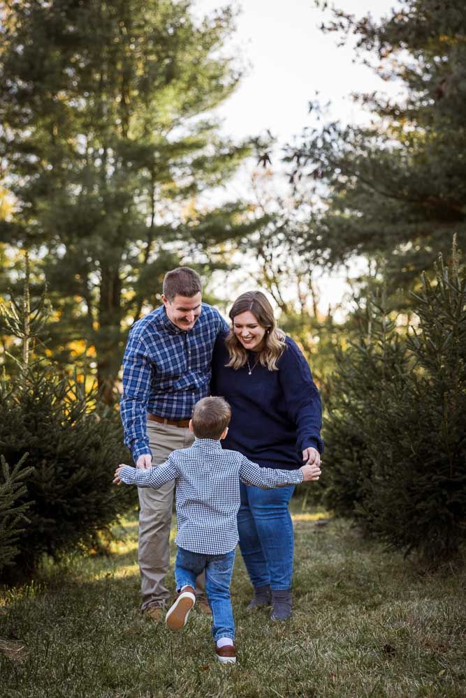 A family plays and laughs together while walking through an evergreen tree farm at sunset.