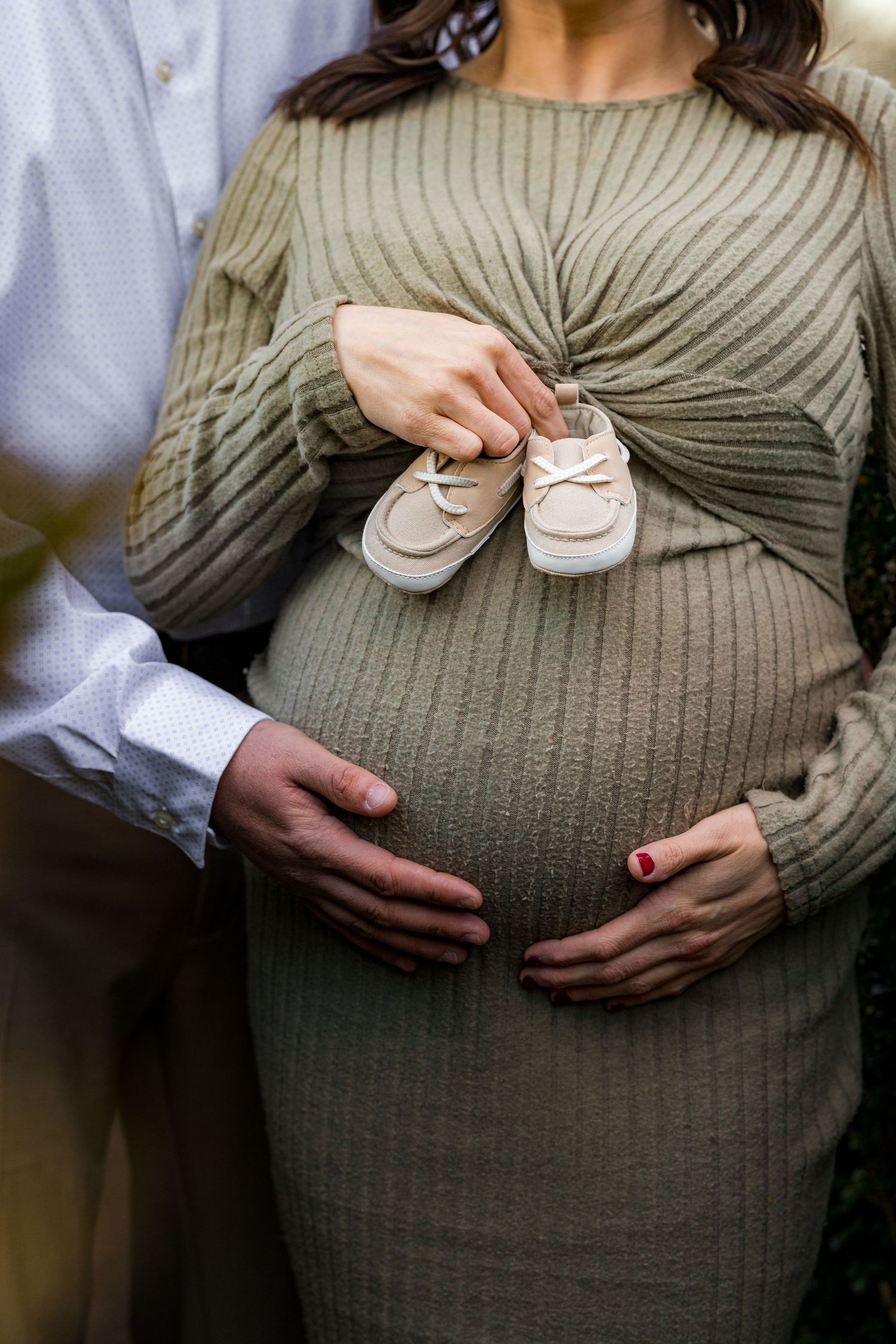 Pregnant couple cradling baby bump with baby shoes during maternity photo session at Smithville Park in Burlington County, NJ