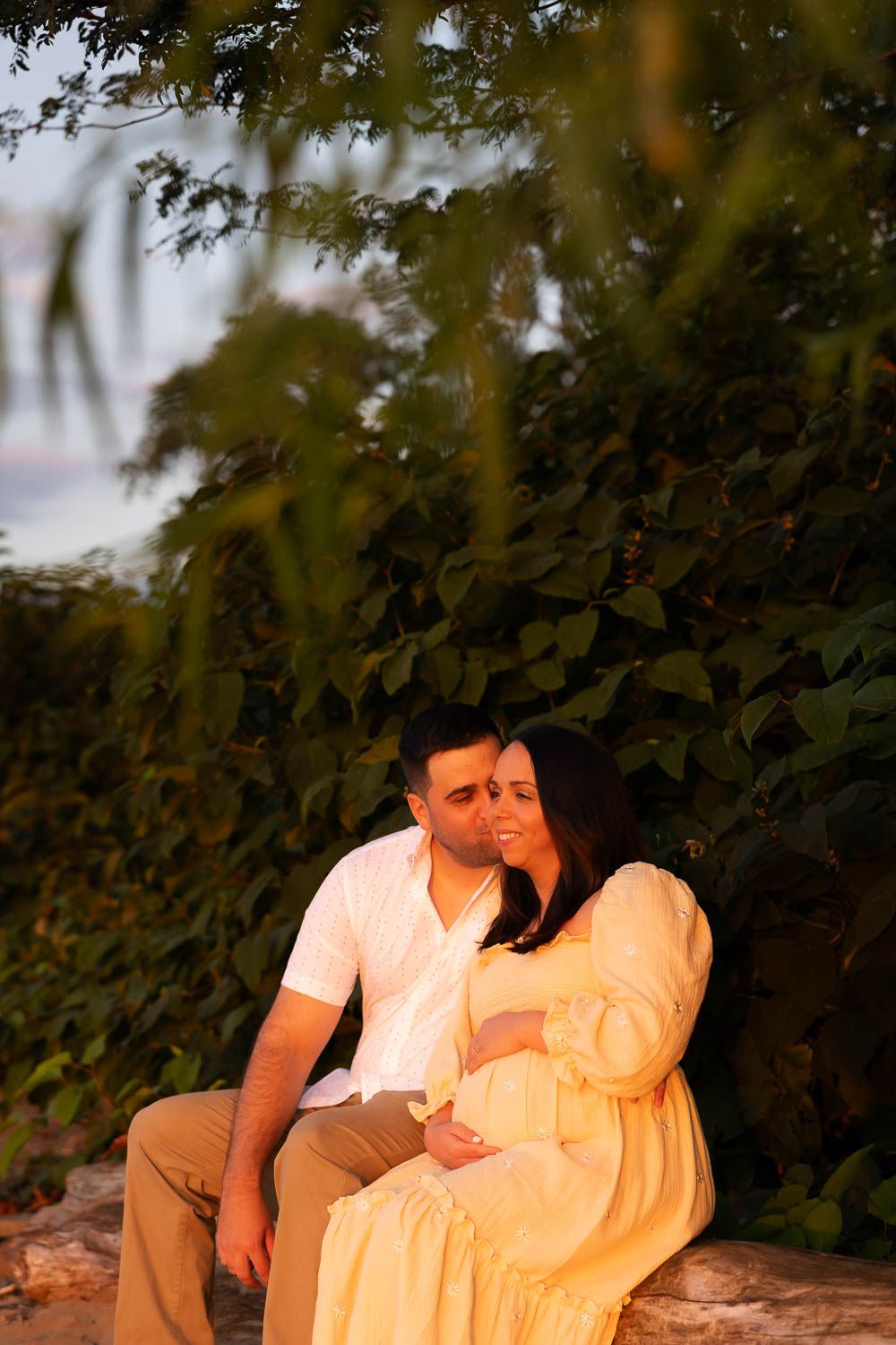 Couple enjoying intimate moment during golden hour sunset maternity session along the waterfront at Palmyra Nature Cove in Palmyra, NJ