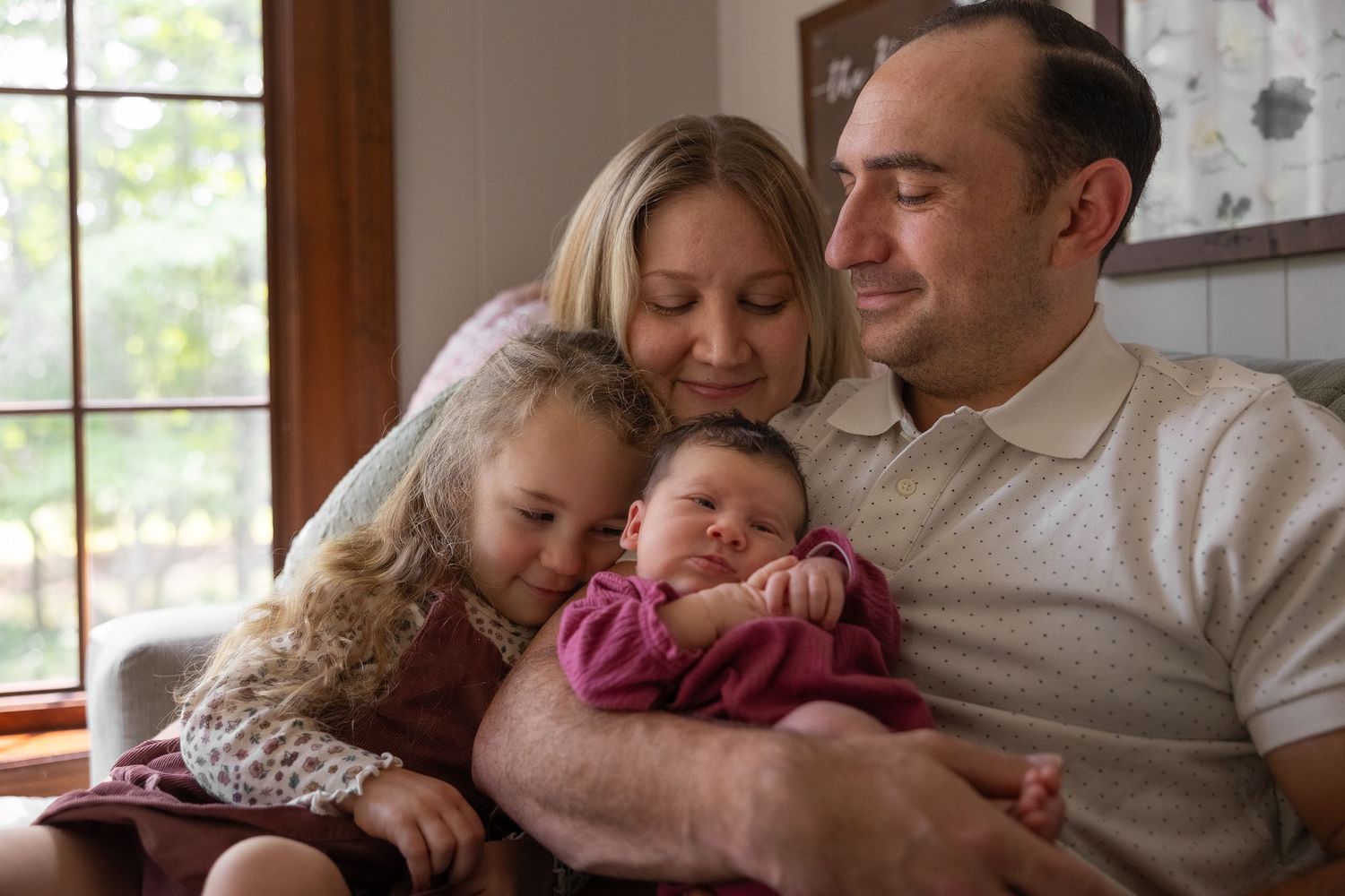 Family cuddling and holding newborn baby during lifestyle newborn photo session in Mercer County, New Jersey, by Rego Photography