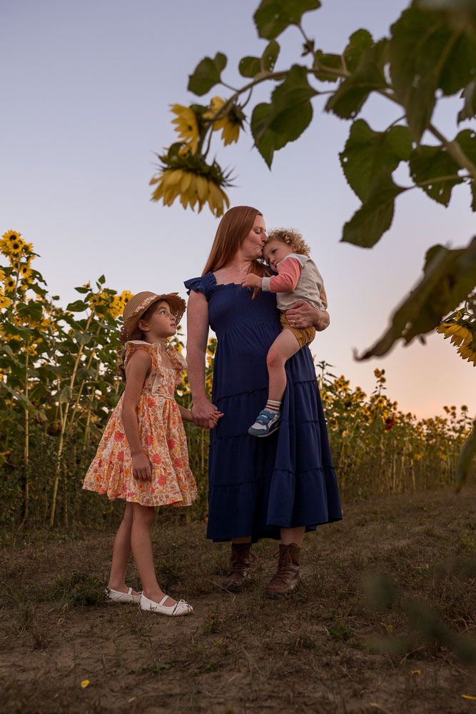A tender family moment in a sunflower field at sunset, with a navy blue dress and floral dress against golden blooms.
