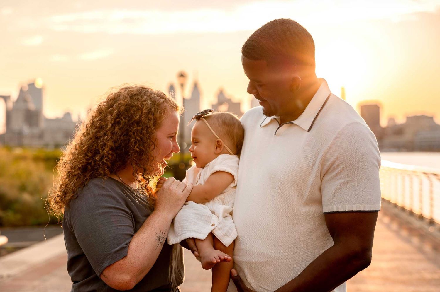 Family with small baby smiling during golden hour session in Camden County, NJ at waterfront park by Rego Photography