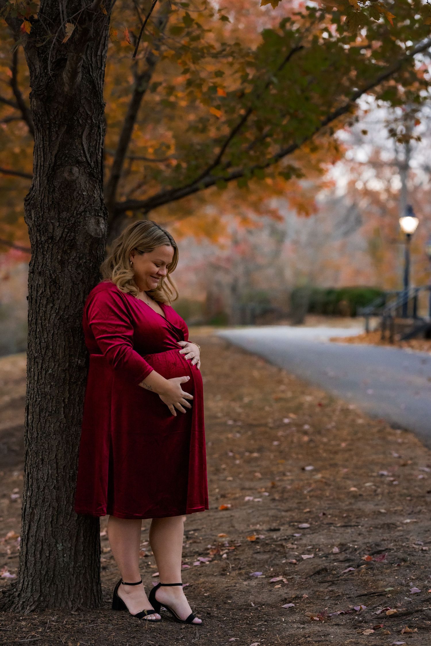 Expectant mother cradling bump during fall maternity session at Smithville Park in Burlington County, New Jersey, by Rego Photography