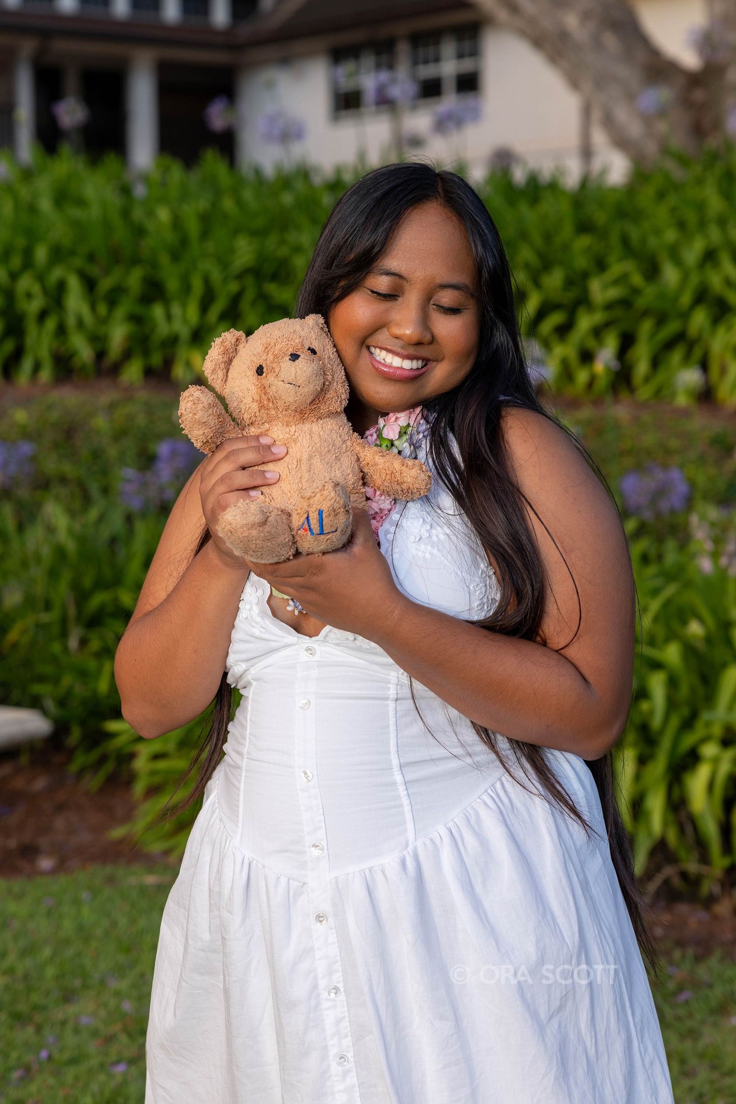 girl holding a teddy bear and wearing a white dress at her high school senior session at Seabury Hall in upcountry Maui