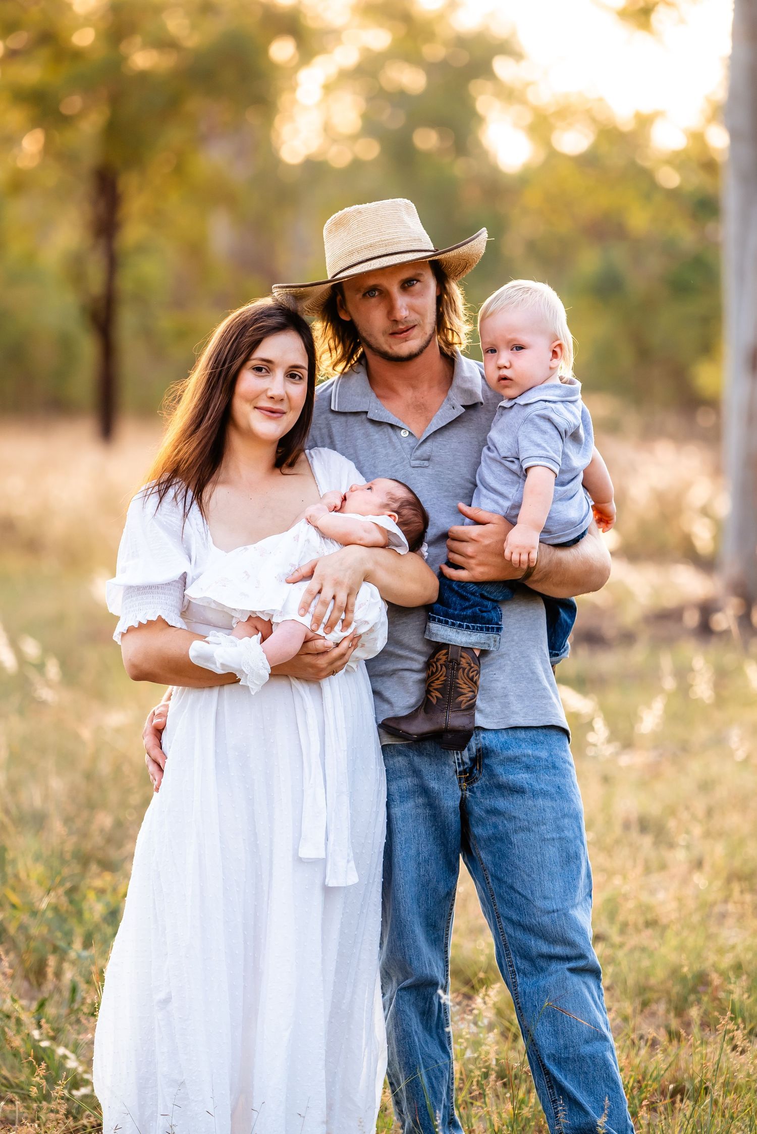A family of three wearing casual attire embraces in a sun-drenched meadow during golden hour.