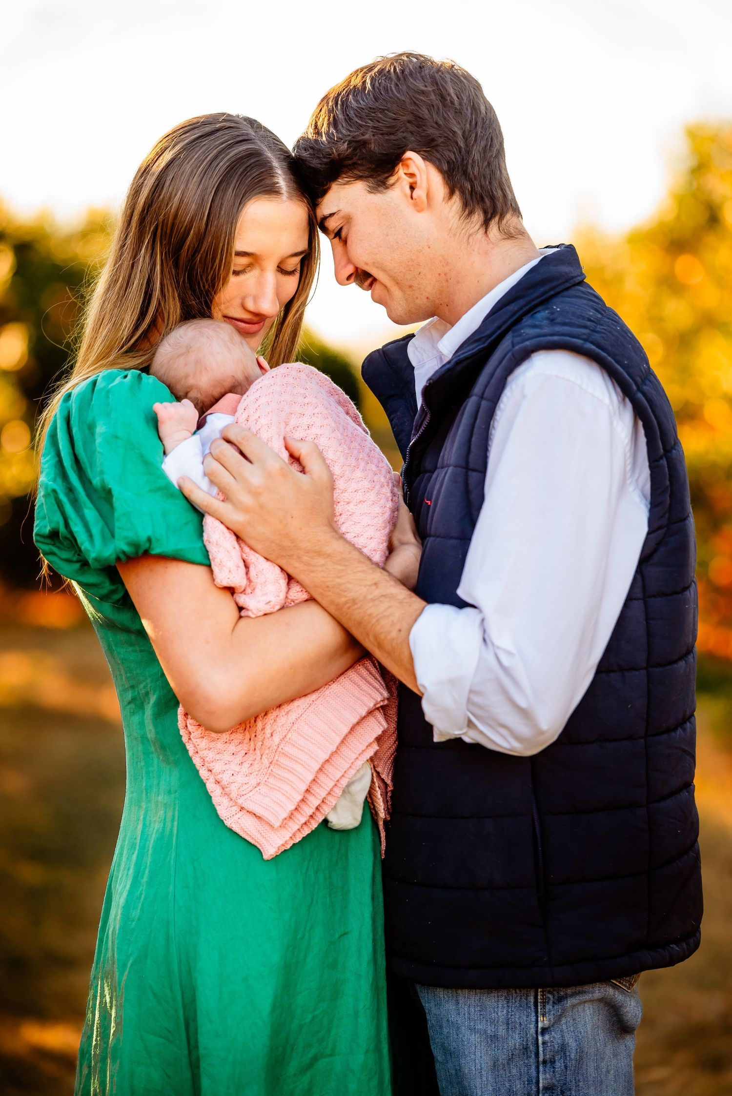 A couple embraces in a sunset photoshoot, the woman wearing a vibrant green dress and the man in a blue shirt.