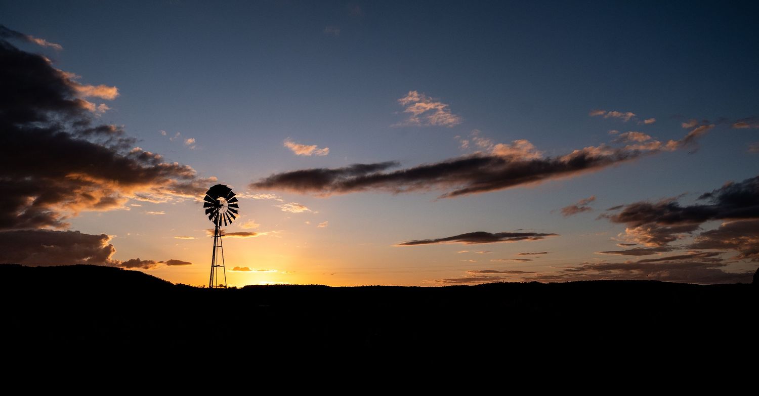 A dramatic sequence of sunset silhouettes against an orange sky with windmills and clouds in the background.