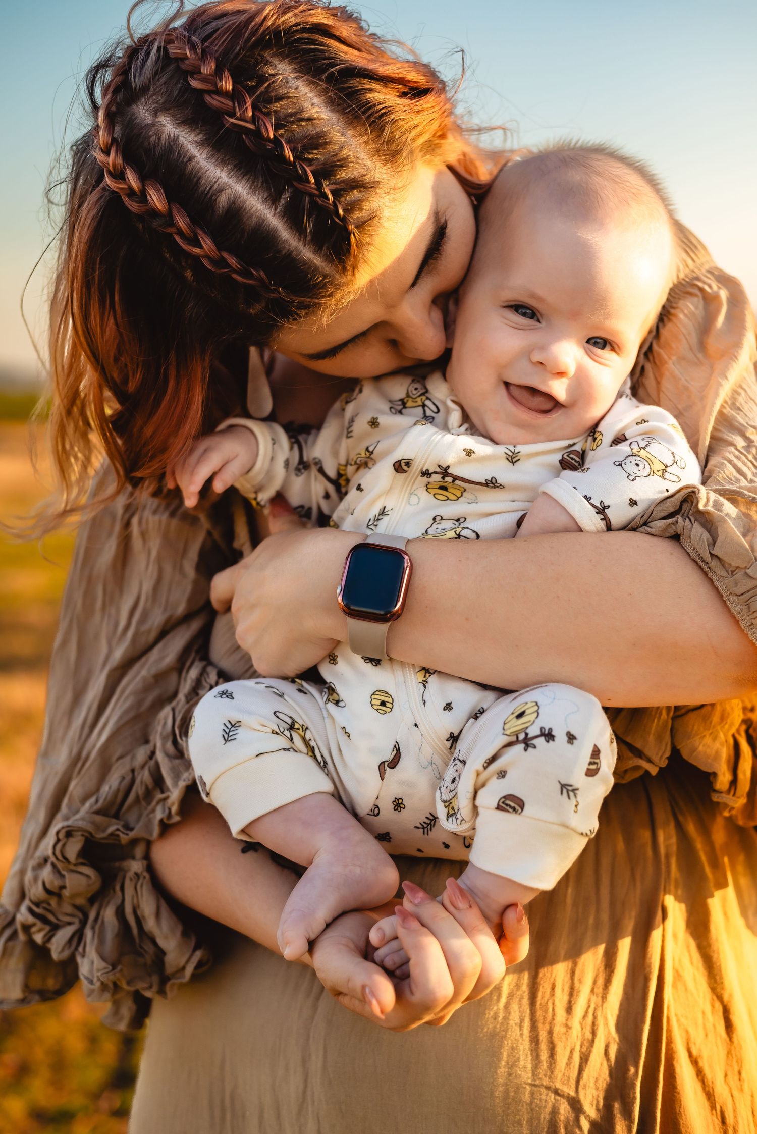 Tender motherhood moment captured during golden hour with baby in patterned onesie.