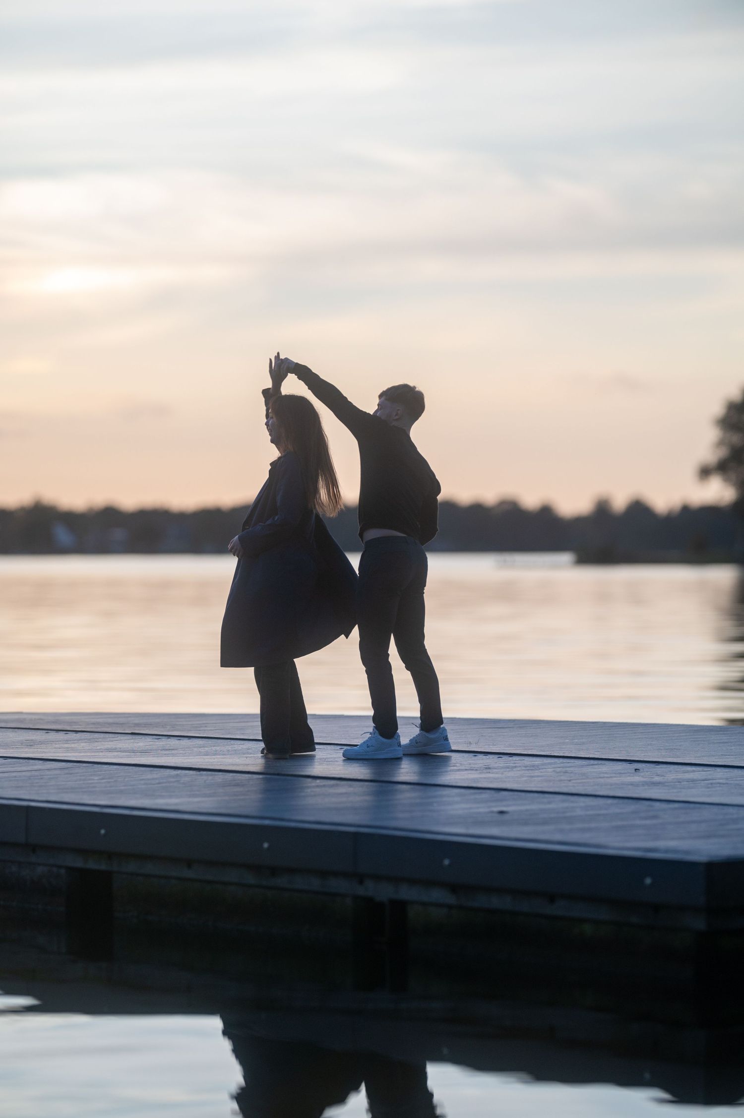 Couple dancing silhouetted on a wooden dock at sunset over a calm lake.