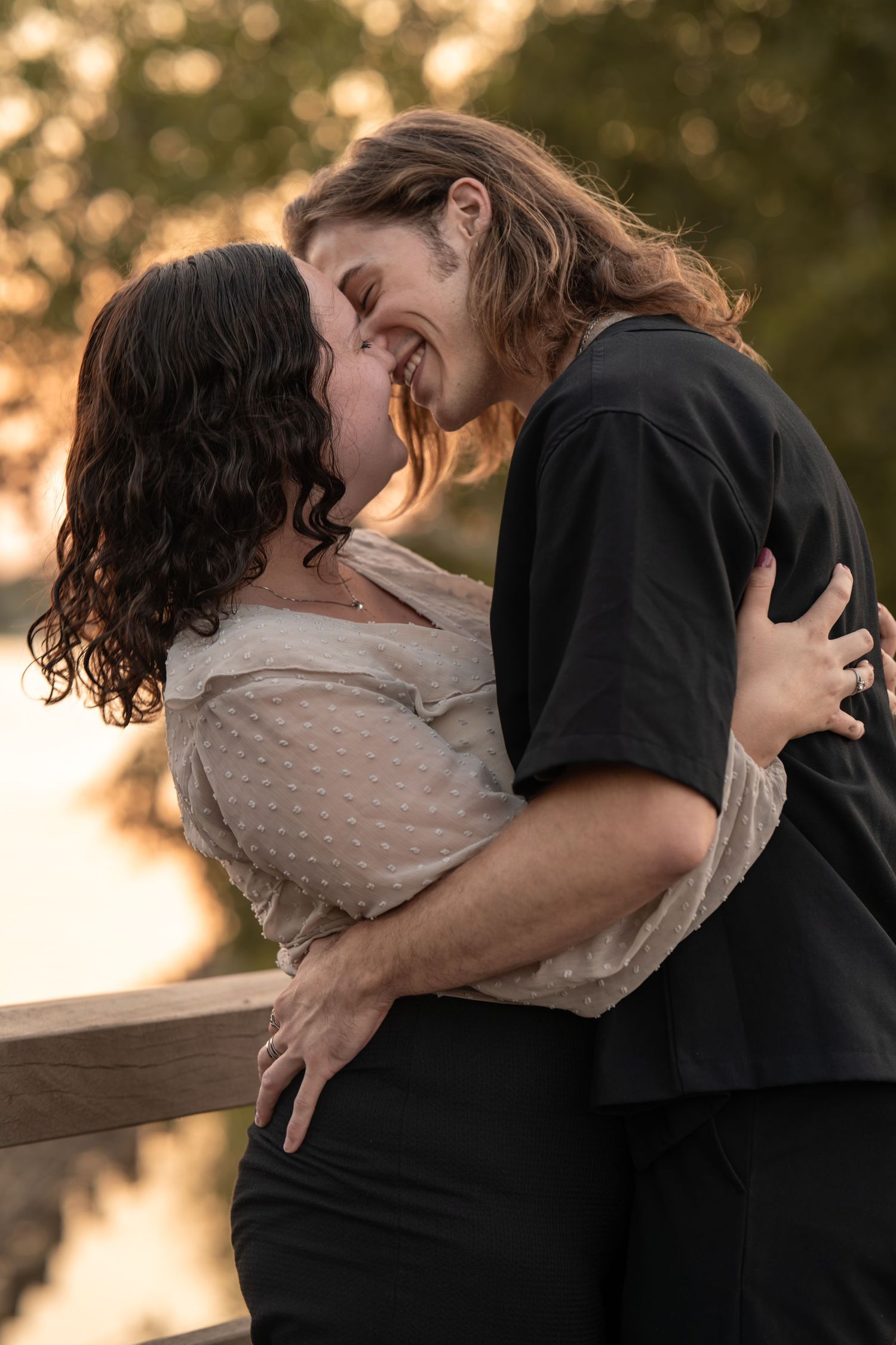 Laughing couple embracing and almost kissing on a bridge at sunset in warm golden light.