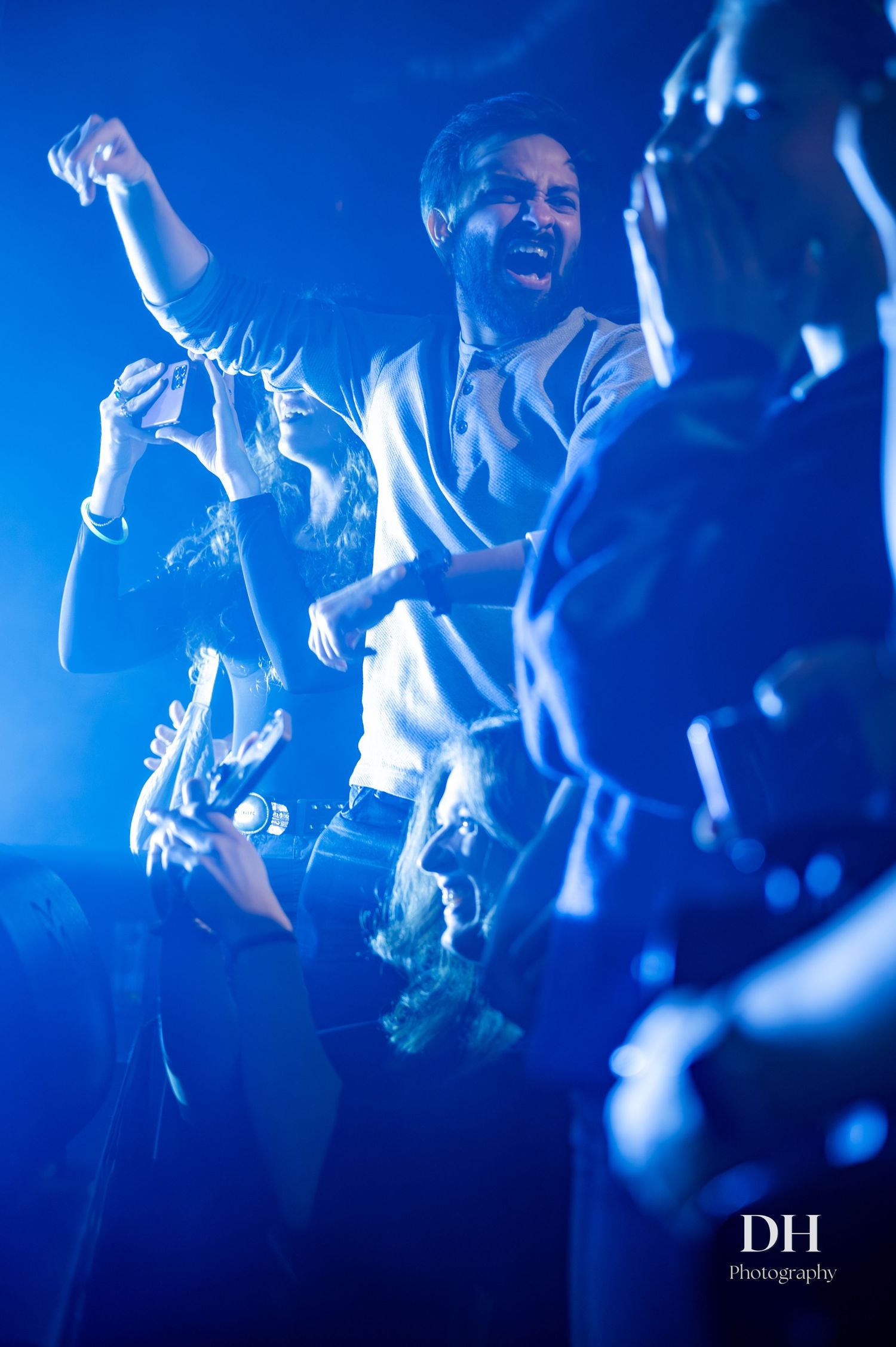 Energetic concert crowd dancing under blue stage lights with performer singing passionately at live music event.