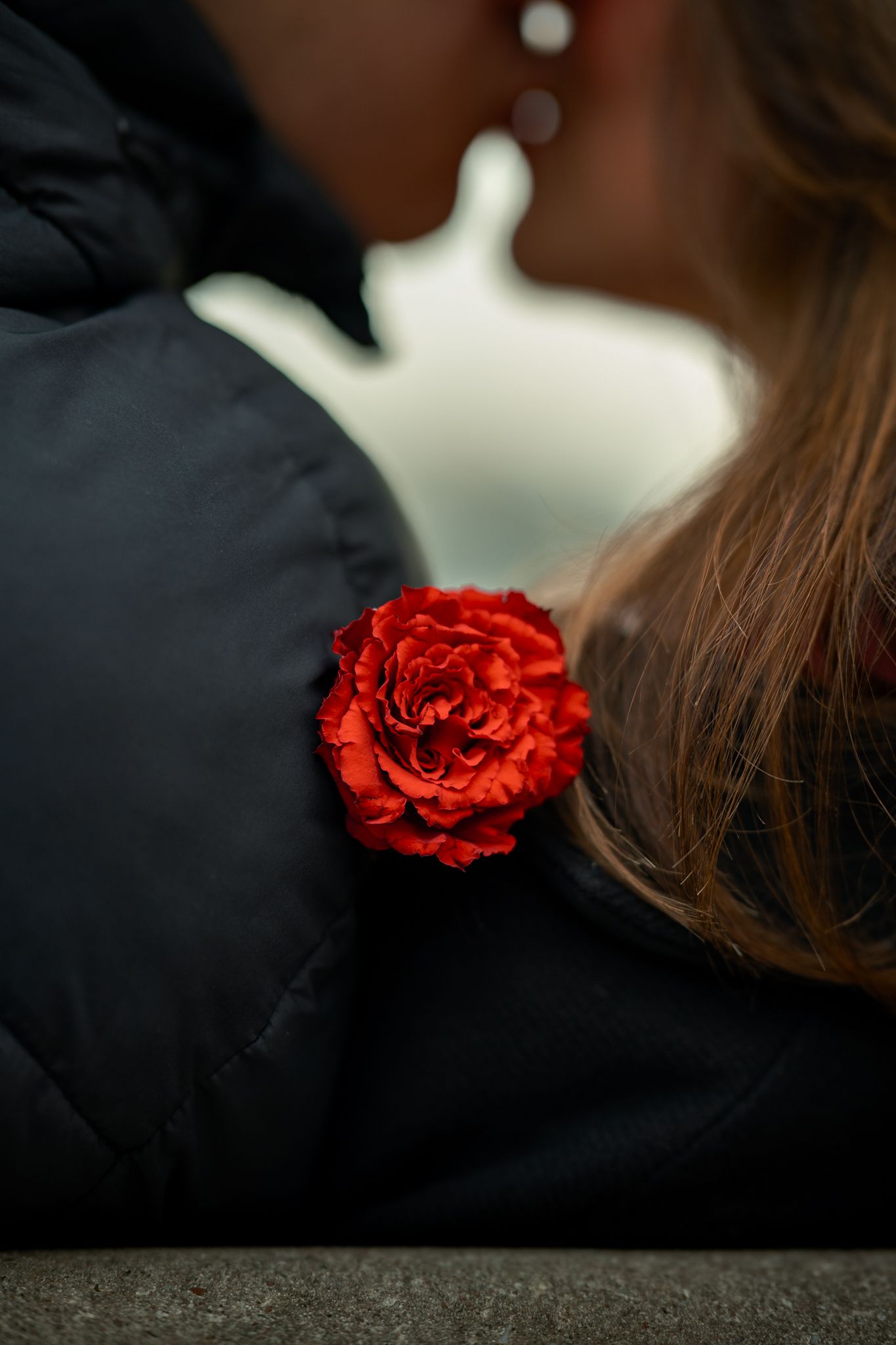 Close-up of a red rose pinned to a black jacket as a couple shares a romantic moment.