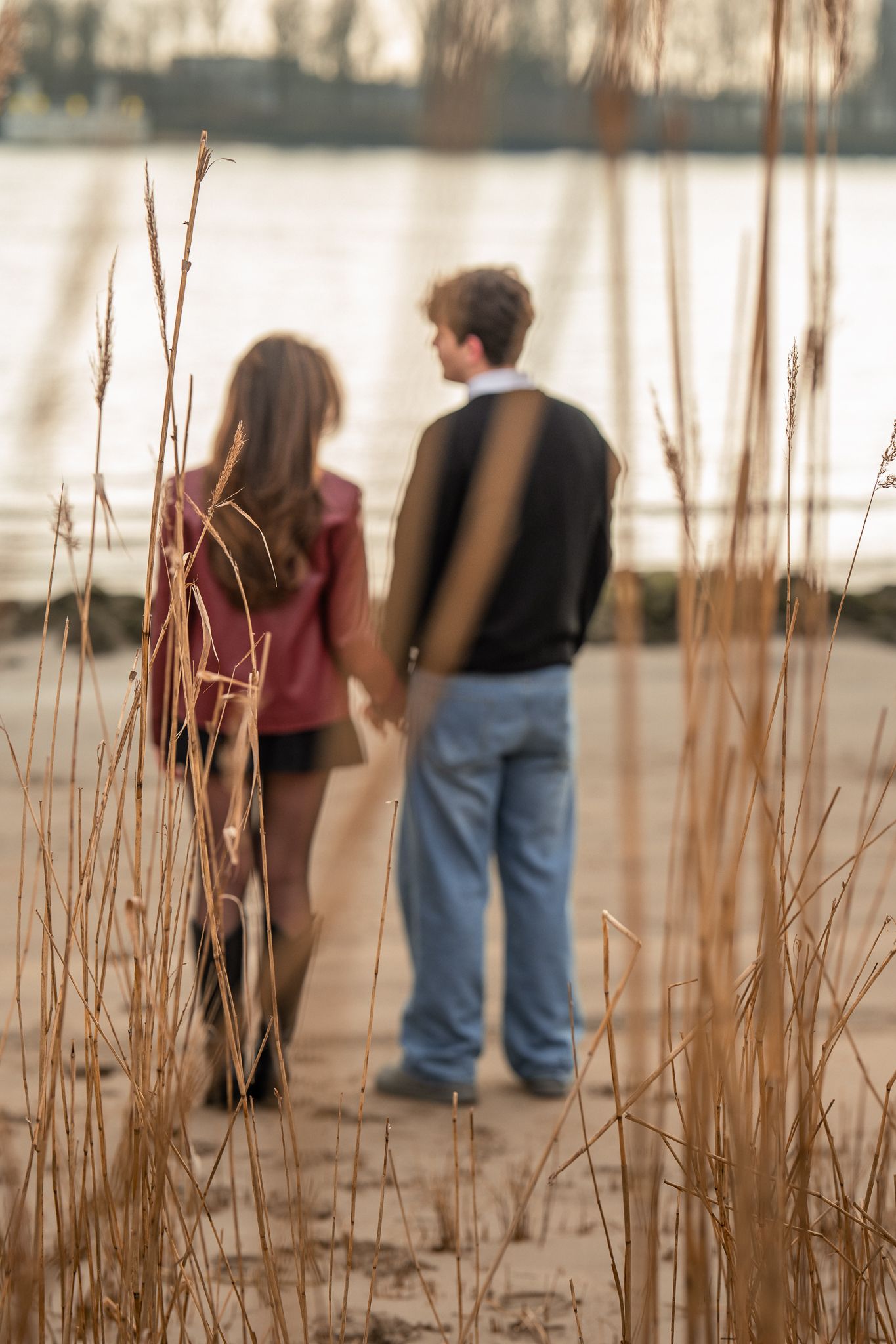 Blurred romantic couple holding hands near a lake shore surrounded by tall golden reeds.
