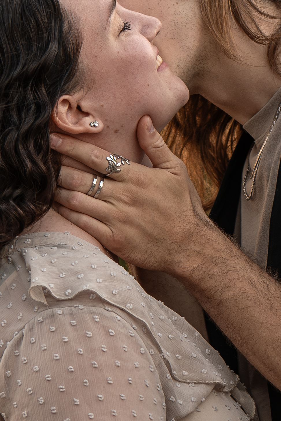 Close-up of a couple almost kissing, hands gently cupping a womans jaw, silver rings visible.