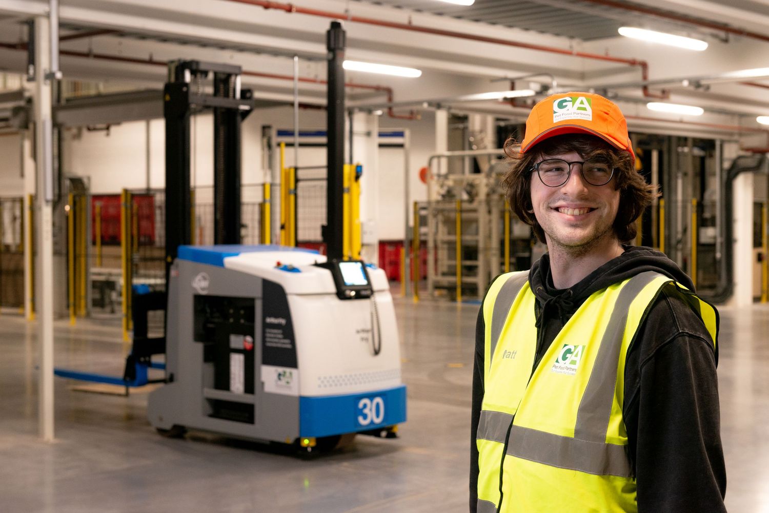 Young apprentice smiling in robot fork lift area of warehouse for manufacturer.