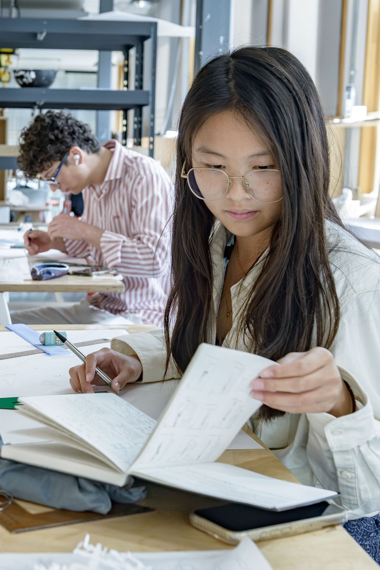 Bartlett School of architecture marketing portrait of female student working at studio desk looking at notebook.