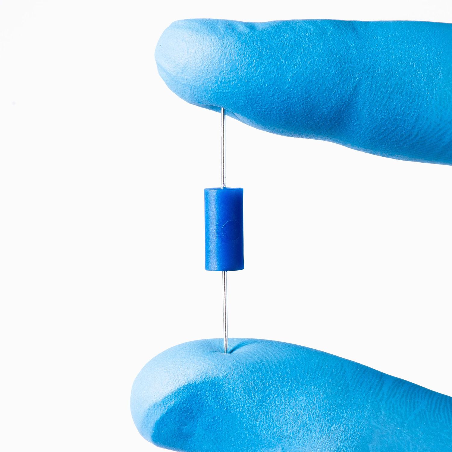 Small cylindrical fuse with wires on each end being held between blue gloved fingers to show scale. Commercial photography for small busines