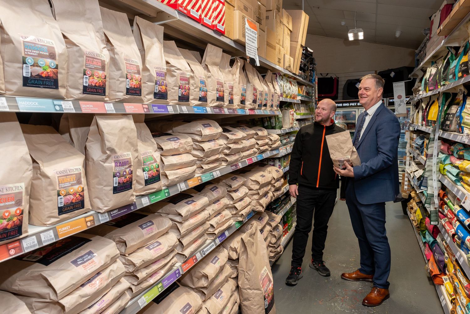 Pet shop owner chats with salesman in aisle of bagged dog food.