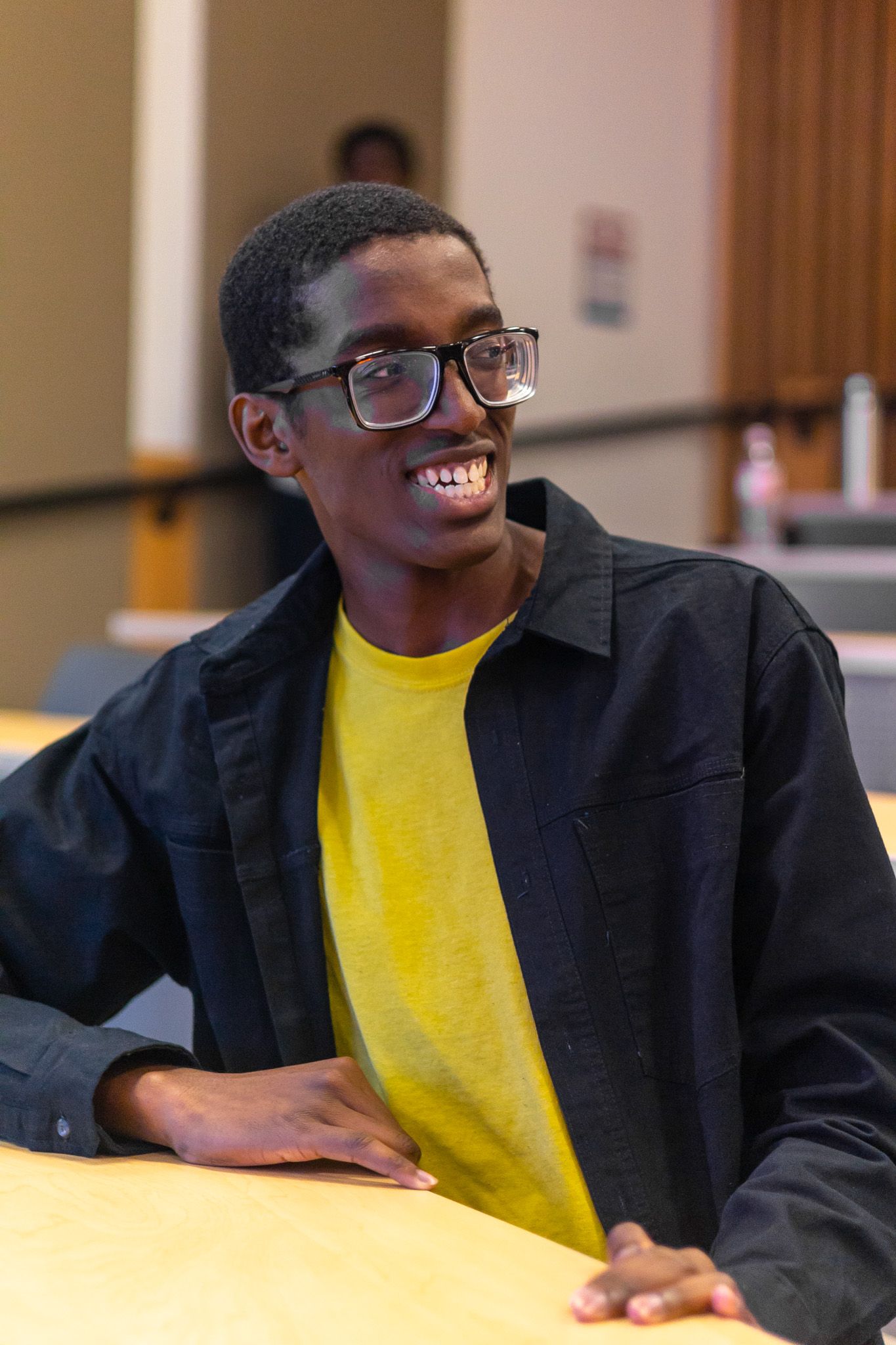 A person in a yellow shirt and black blazer smiles during a presentation.