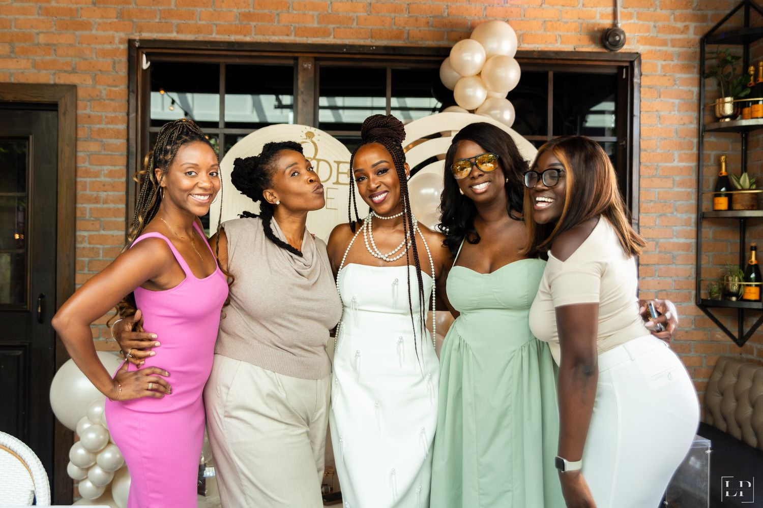 Group photo of friends in pastel dresses ranging from pink to mint green at a celebration.