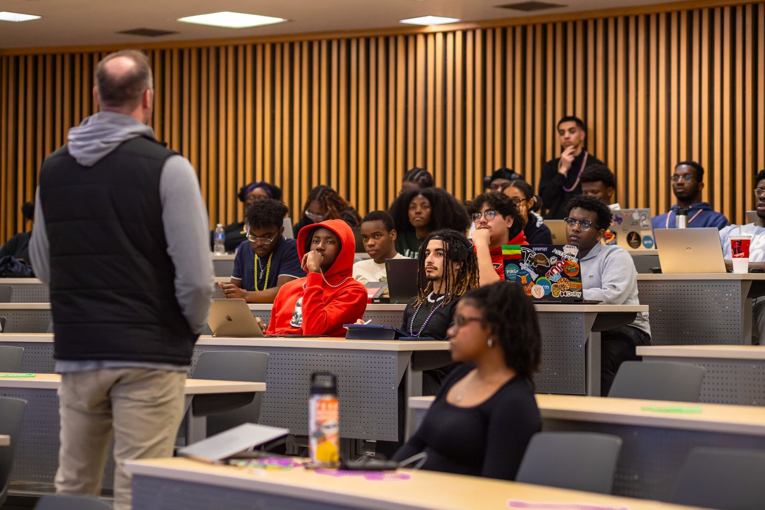 Students gather in a modern classroom with wood paneled walls and fluorescent lighting for a presentation.