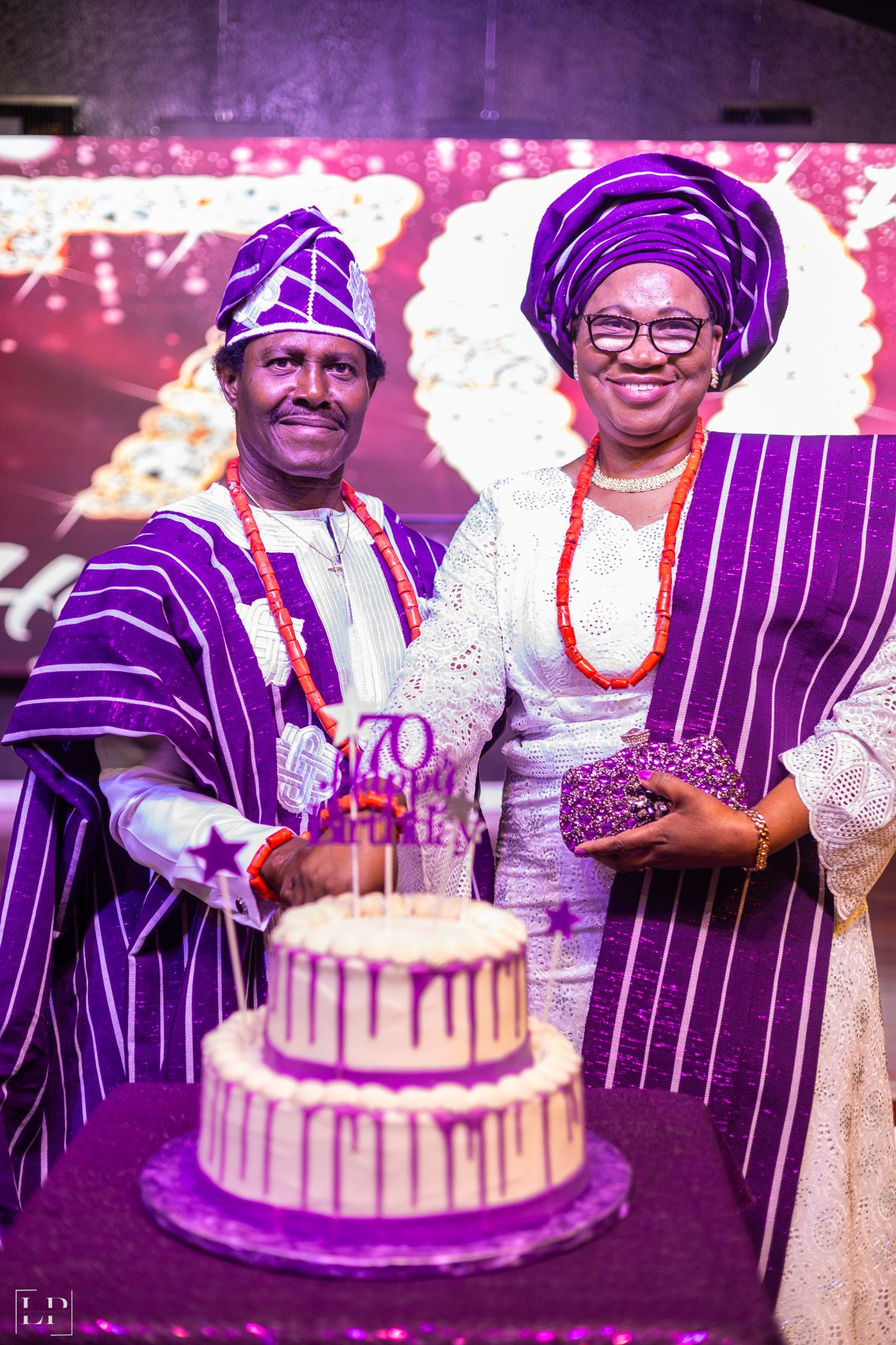 Traditional African wedding cake cutting moment with couple in matching purple and white attire.