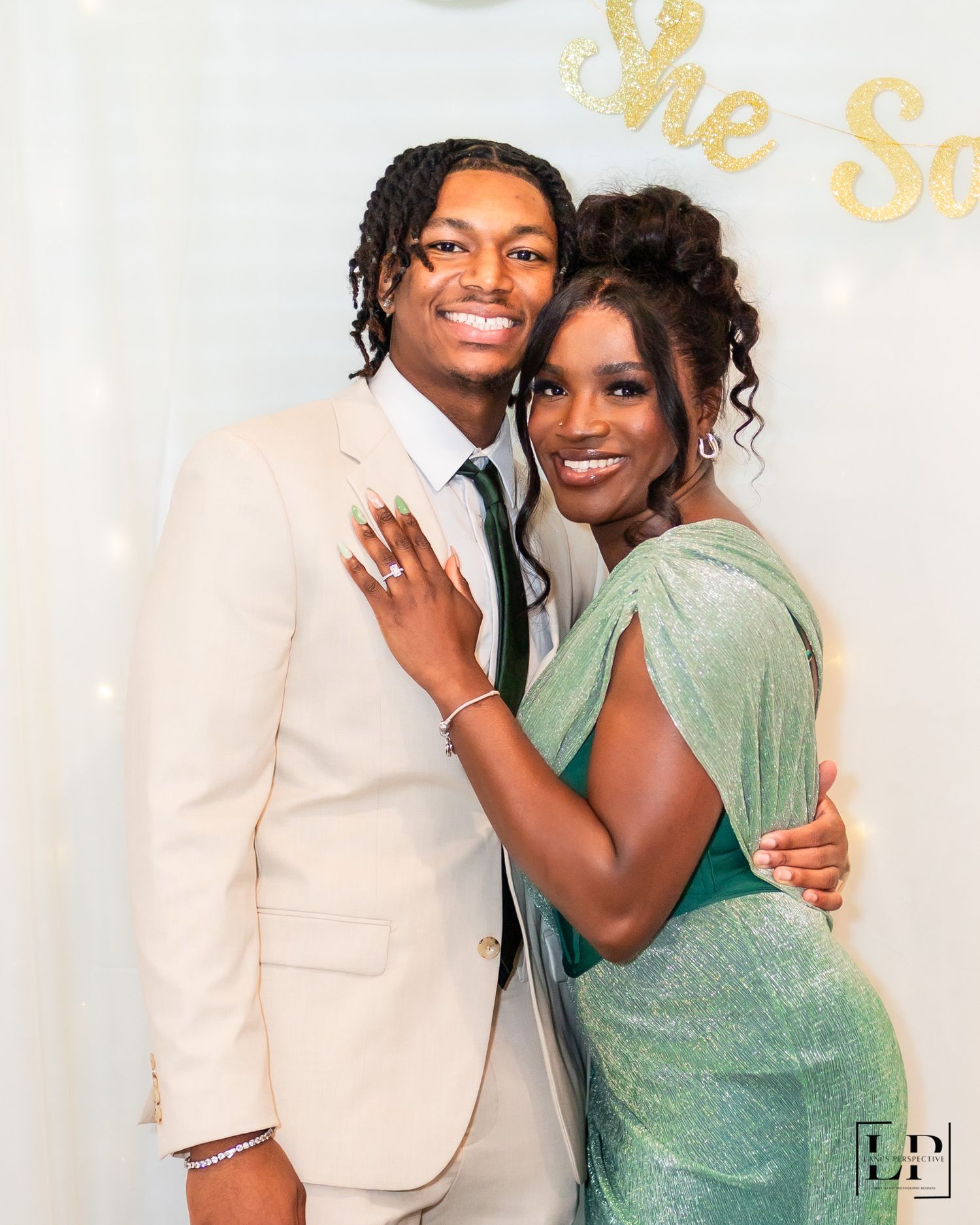 Couple poses together at a formal event, with one wearing a cream suit and the other in a mint green dress.