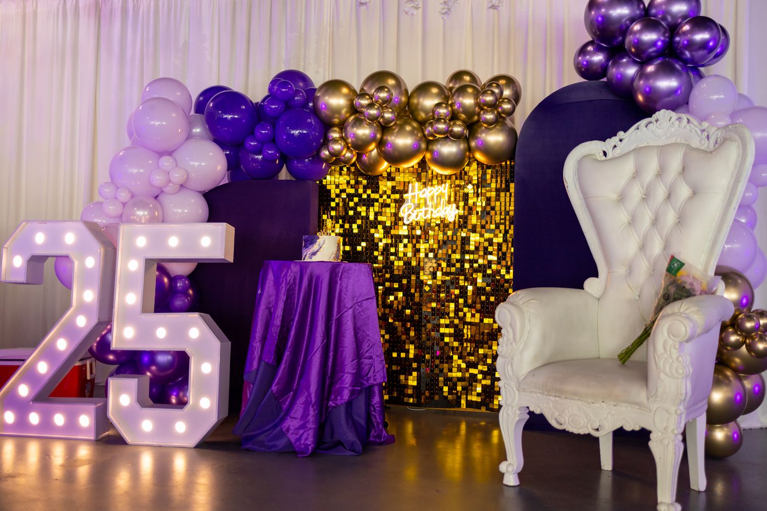 Purple and gold party decor with balloons, throne chairs and illuminated letters.