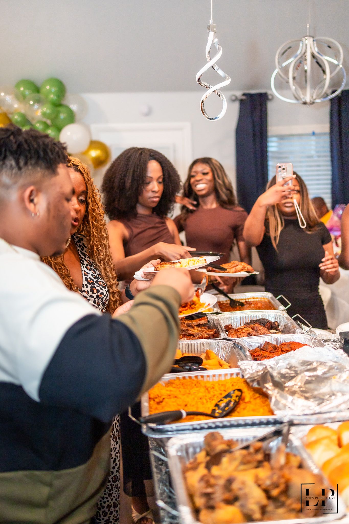 Guests serving themselves from a buffet line filled with various dishes under hanging decorations.