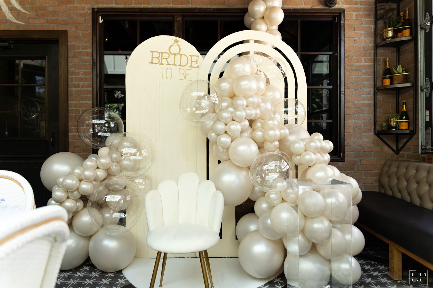 Elegant white balloon arch installation with pearlescent balloons against brick wall.