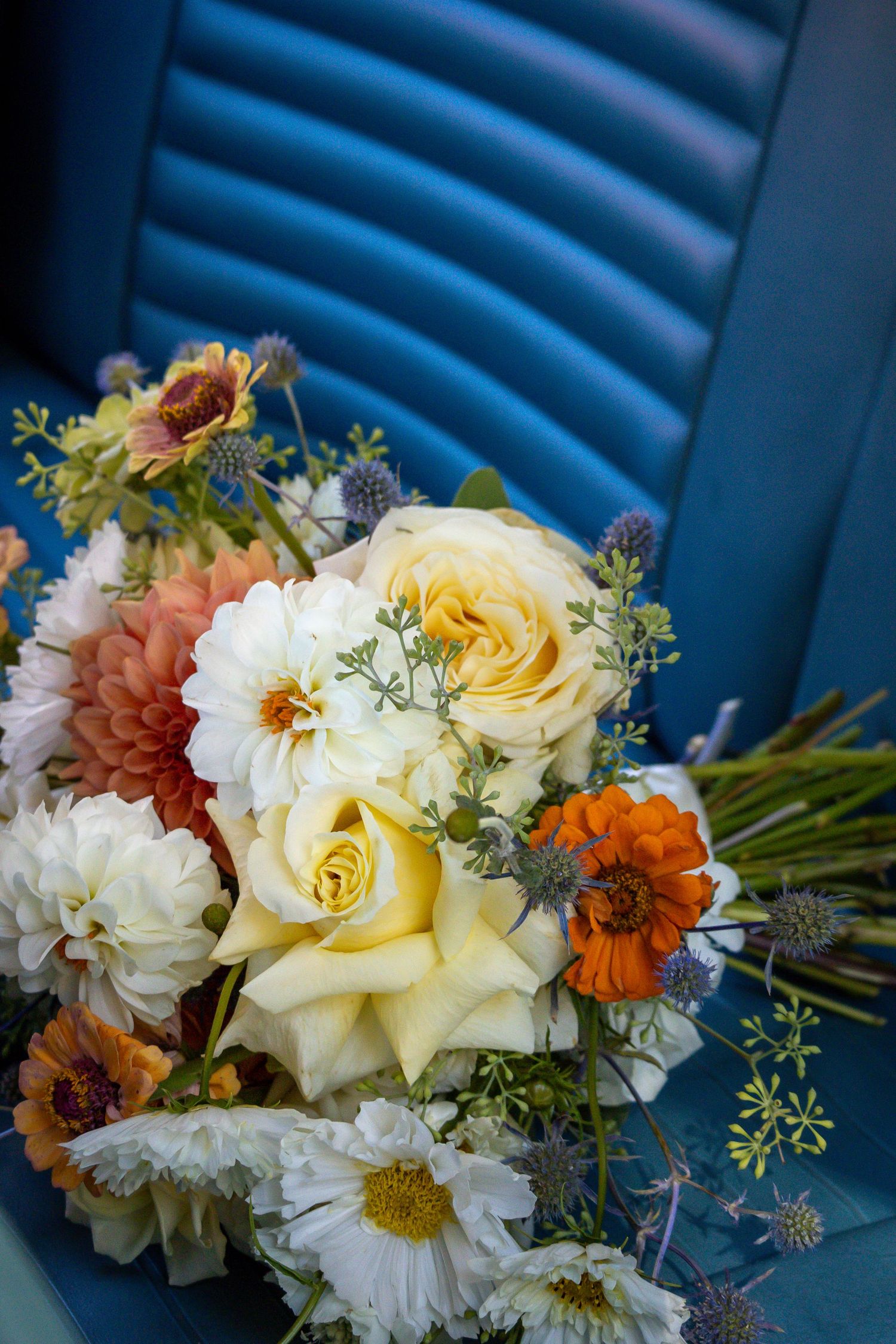 Colorful bridal bouquet with yellow roses, dahlias, and wildflowers on a blue seat.