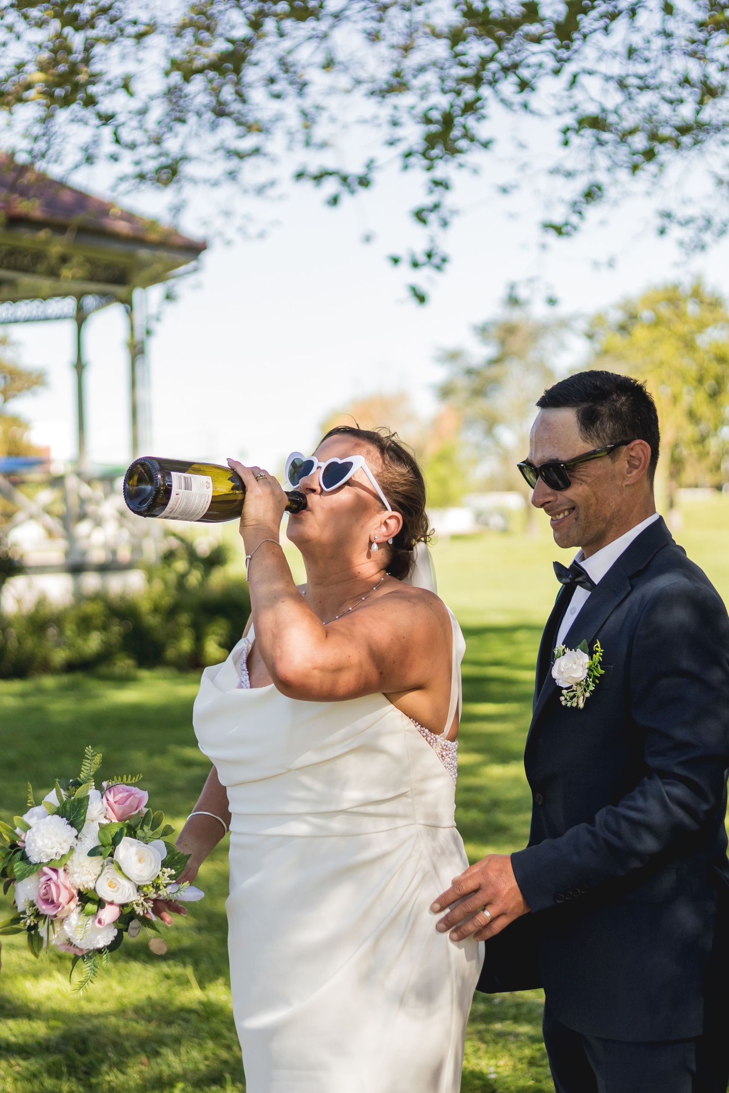 Wedding party drinks champagne and celebrates outdoors on sunny day.
