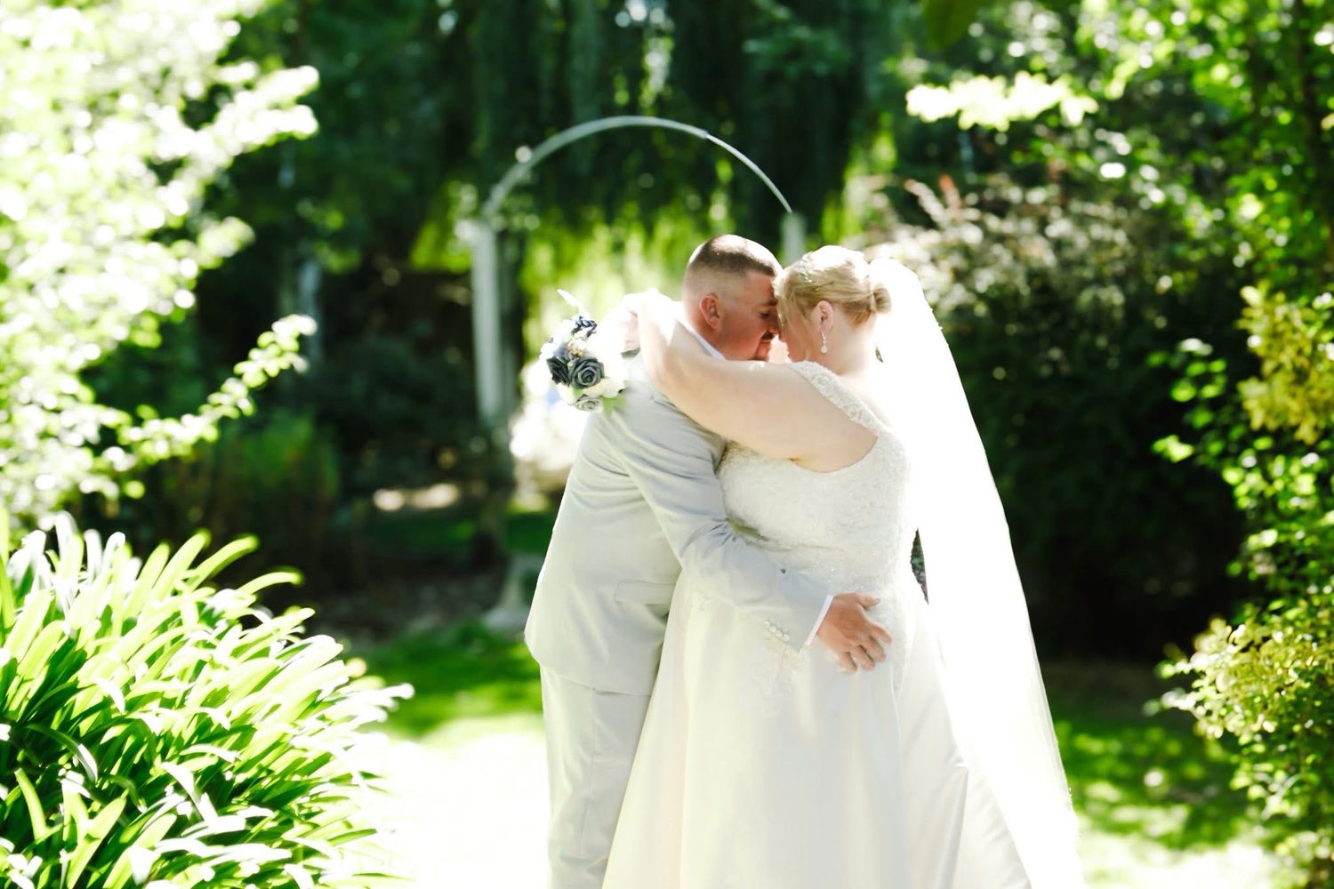 Bride and groom sharing a romantic kiss in a lush garden setting with a floral arch backdrop on their wedding day.