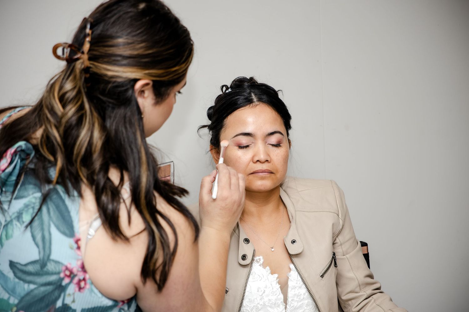 Makeup artist applying foundation to a bride's face during wedding preparations in a bright studio.
