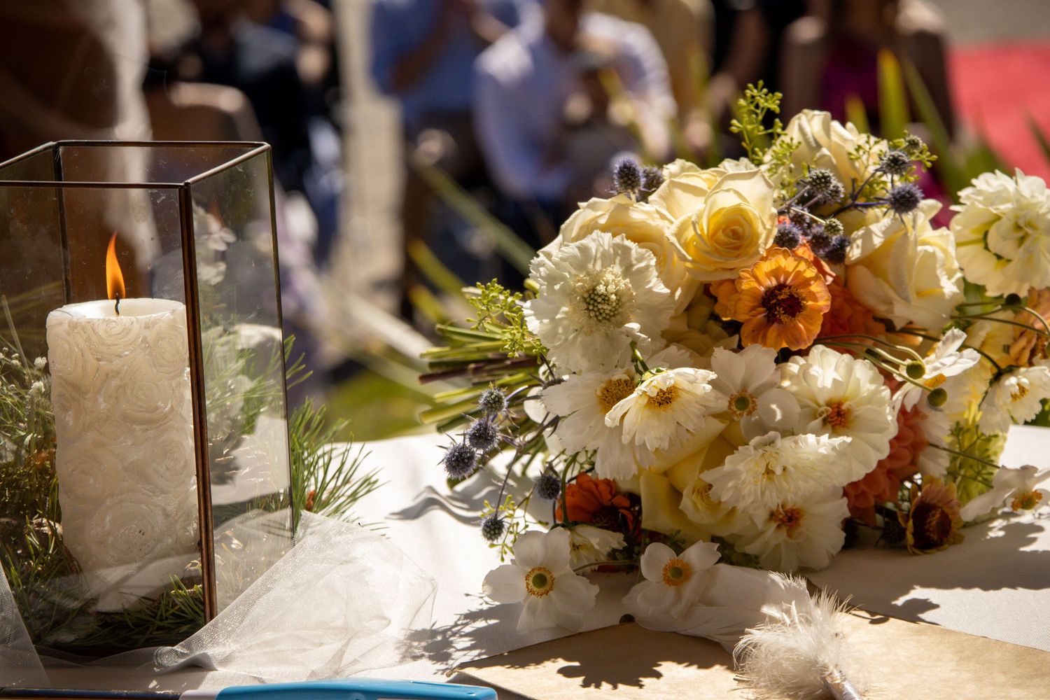 Elegant wedding table with white candle in glass lantern and colorful floral bouquet featuring roses and wildflowers.