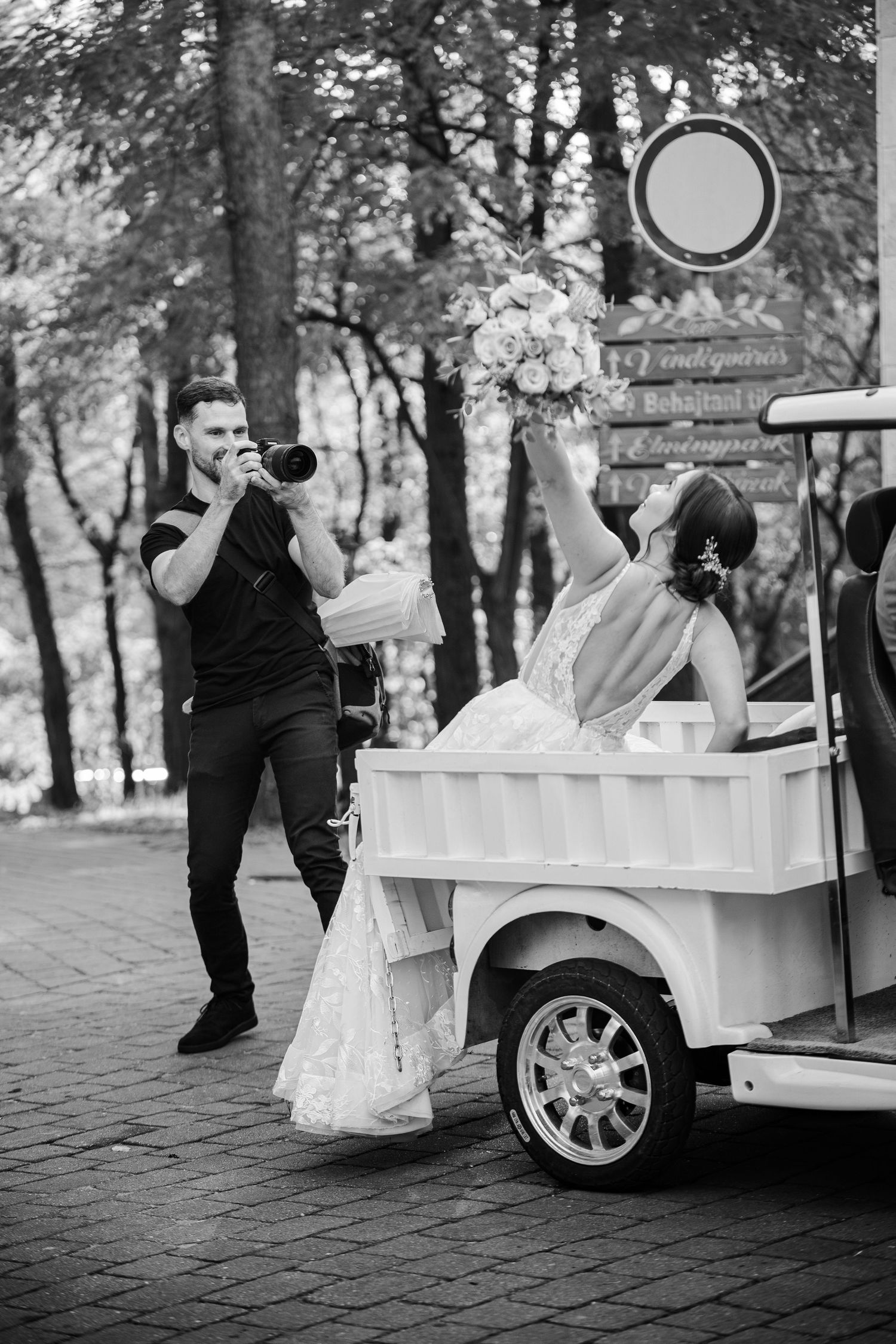 Black and white photo of a wedding photographer shooting near a decorated golf cart.