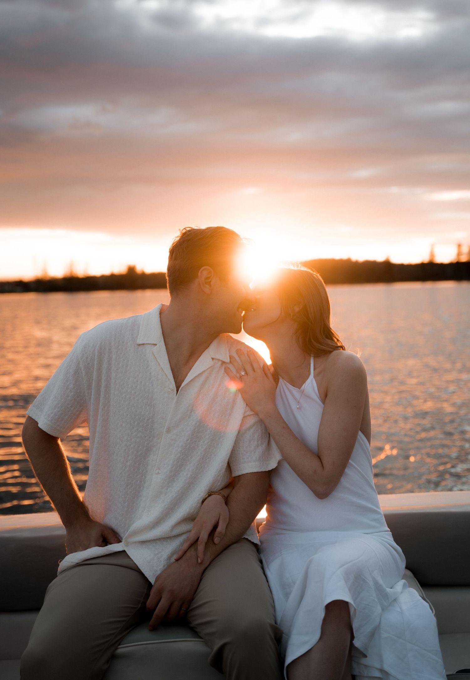 Couple sharing a kiss on a boat at sunset with warm golden light behind them.