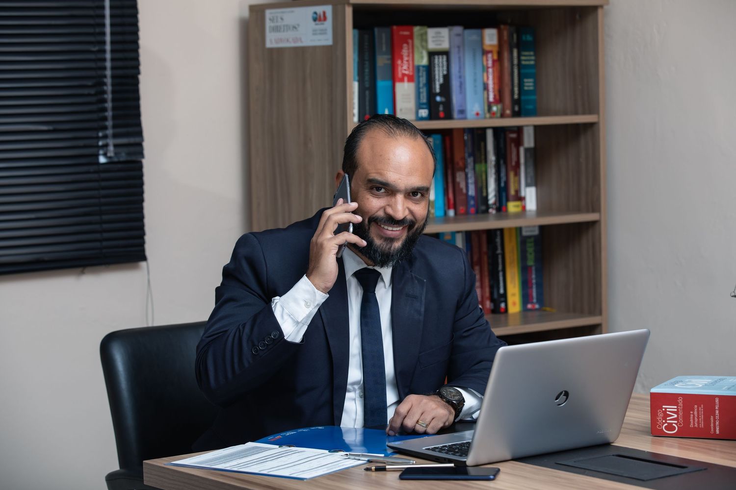 Business professional talking on phone while working at laptop in office.