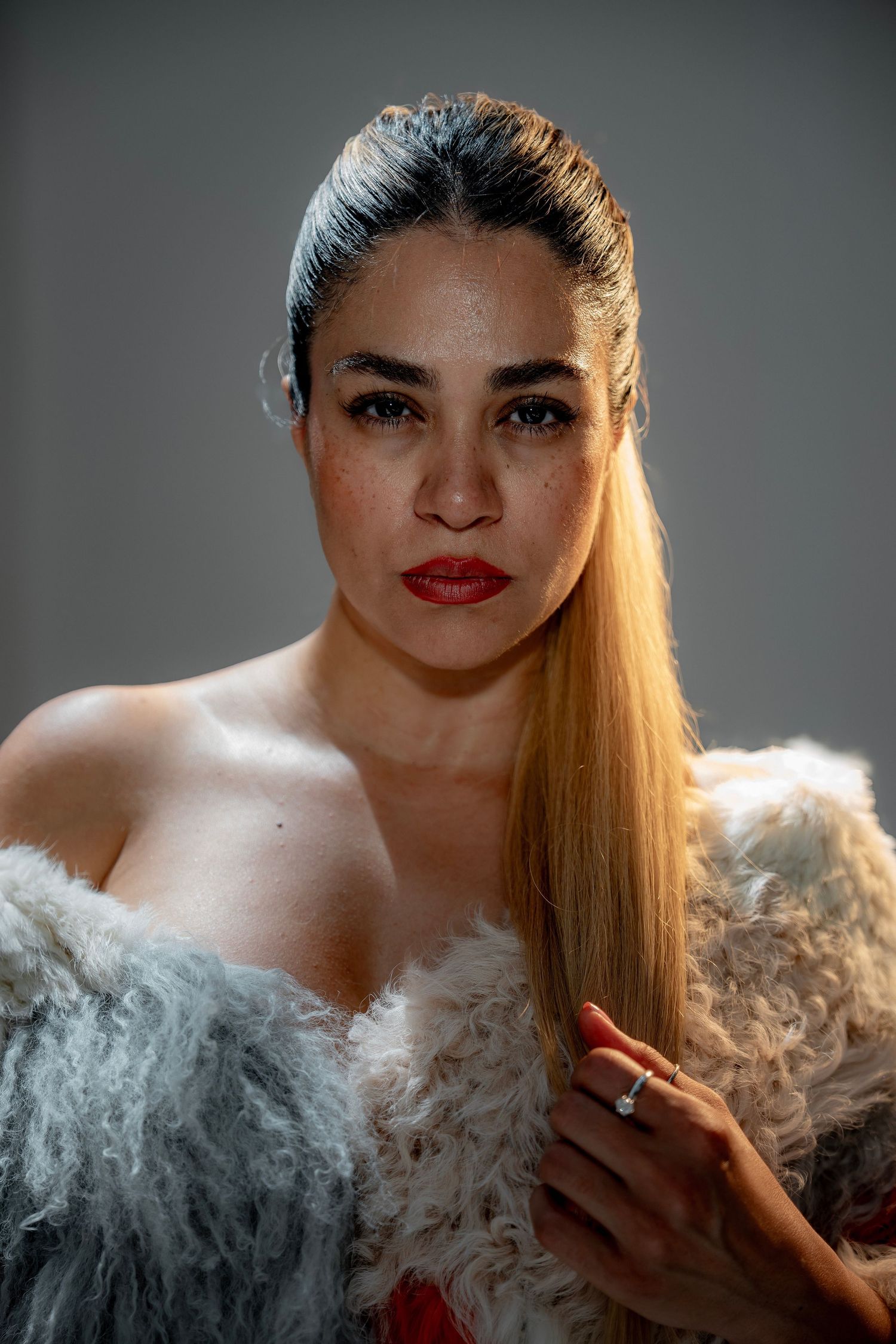 Glamour portrait of model wearing fur wrap with sleek hair and red lipstick against grey background.