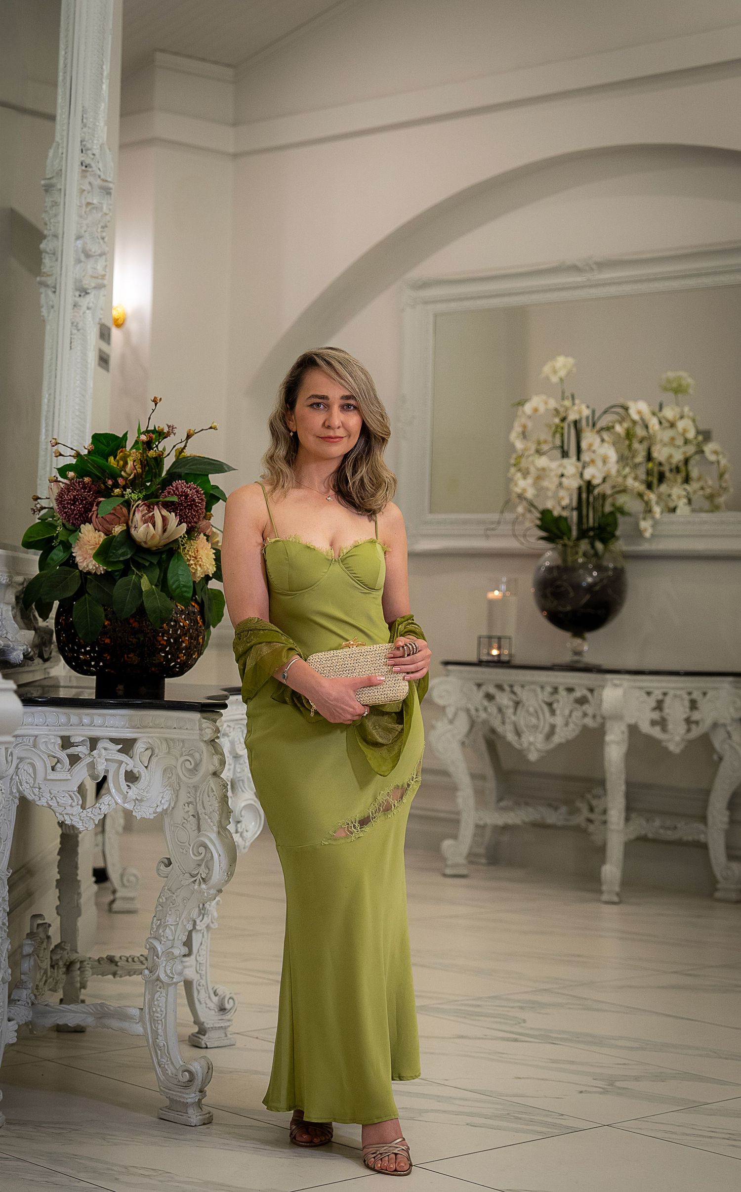 Elegant maternity photos in lime green dress against white interior with ornate furniture.