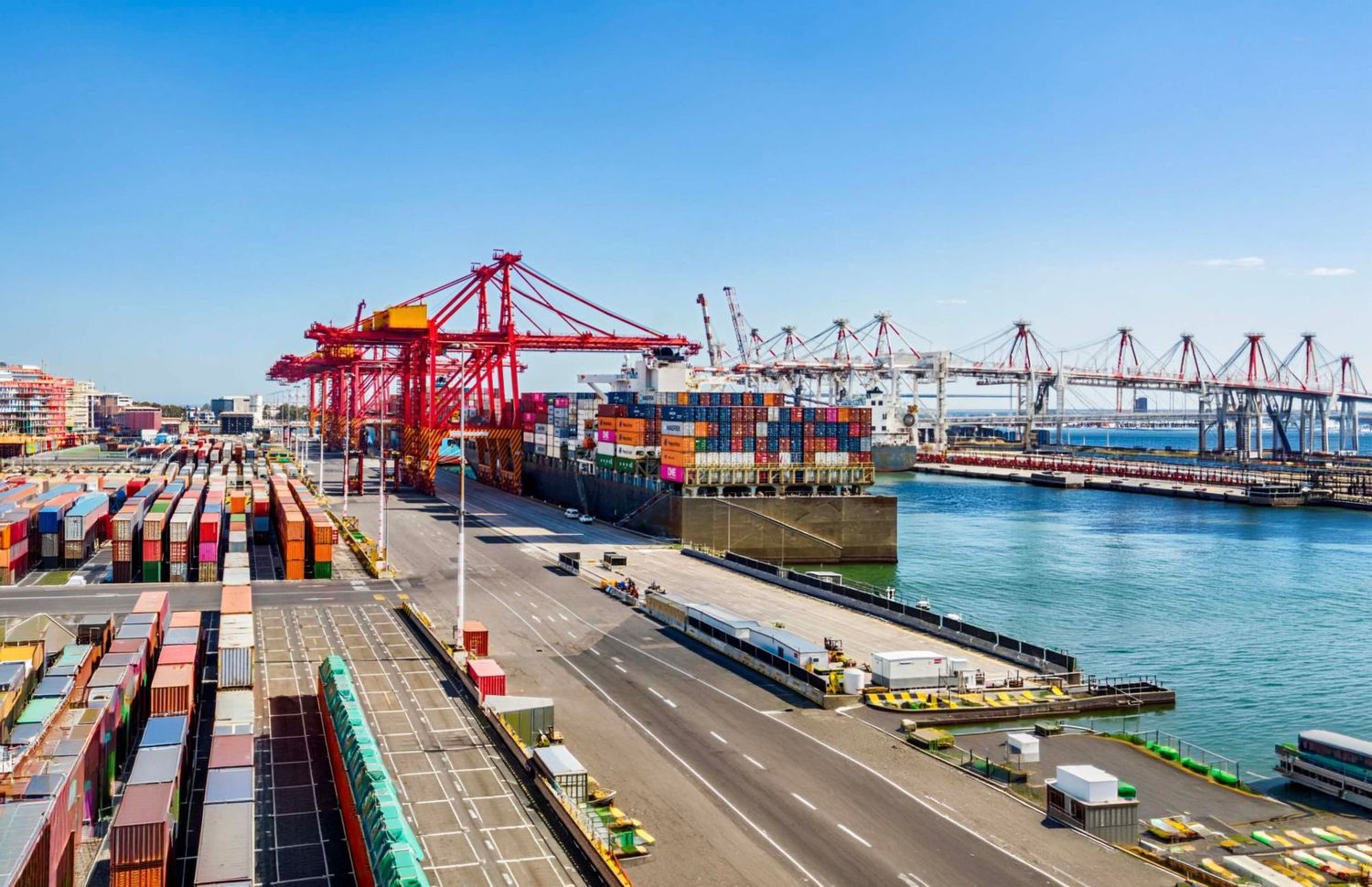 Aerial view of commercial shipping port with red cranes and cargo containers.